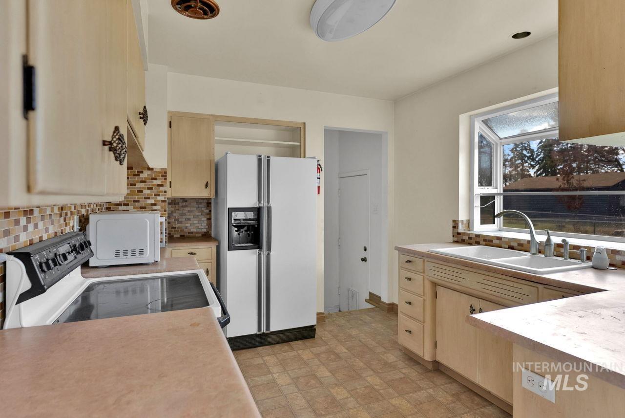 Kitchen featuring light brown cabinets, white appliances, decorative backsplash, and light countertops