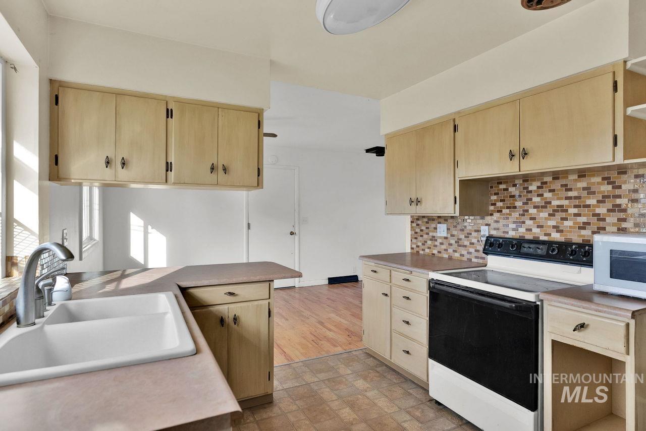 Kitchen featuring electric range, light brown cabinetry, white microwave, and open shelves