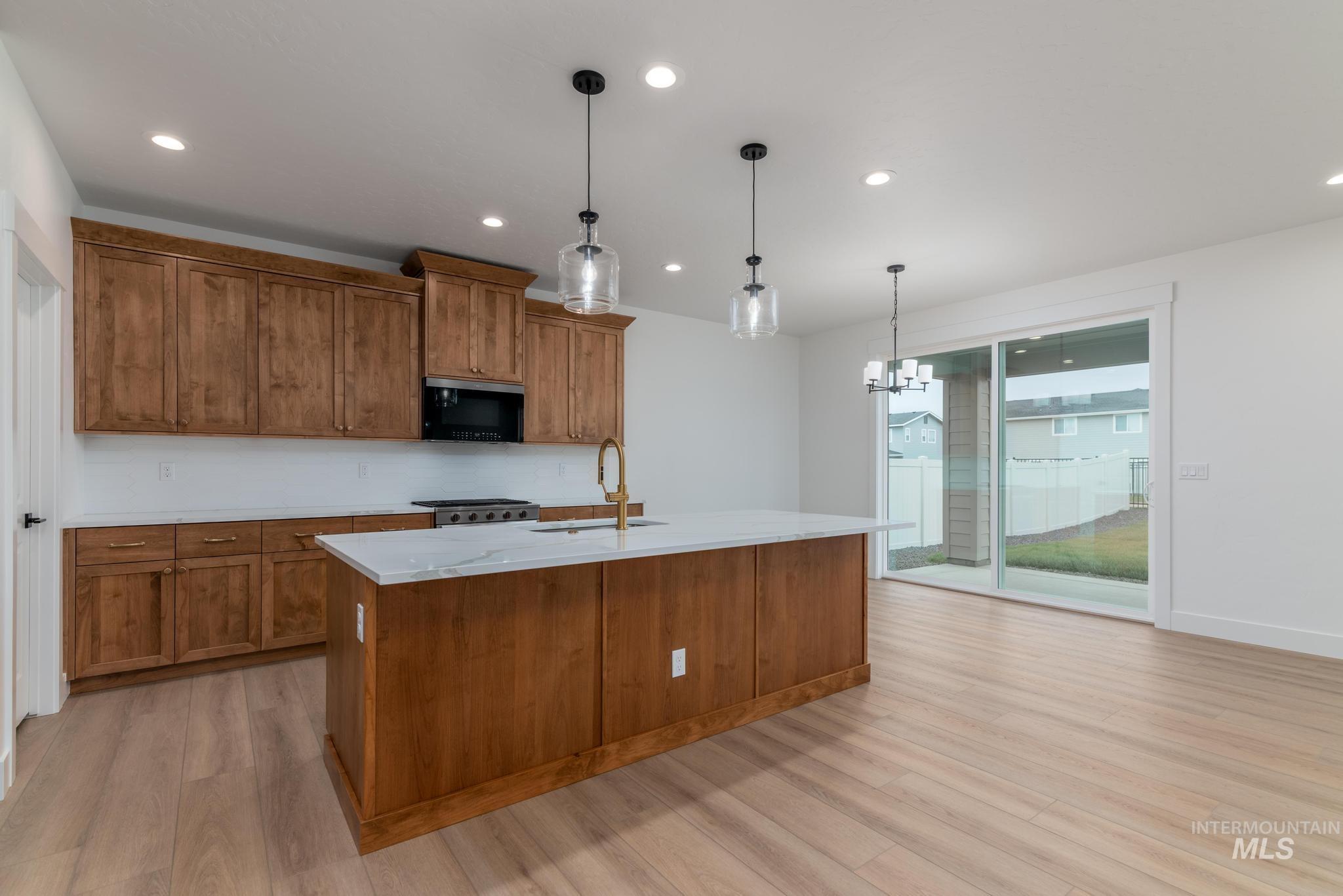 Kitchen featuring brown cabinets, hanging light fixtures, recessed lighting, a center island with sink, and black microwave