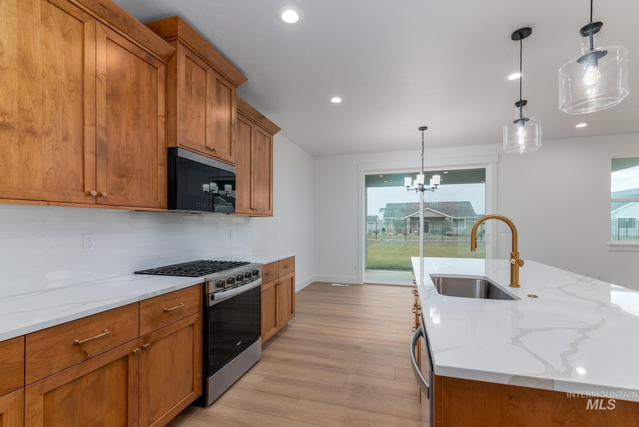 Kitchen featuring brown cabinetry, hanging light fixtures, appliances with stainless steel finishes, and recessed lighting