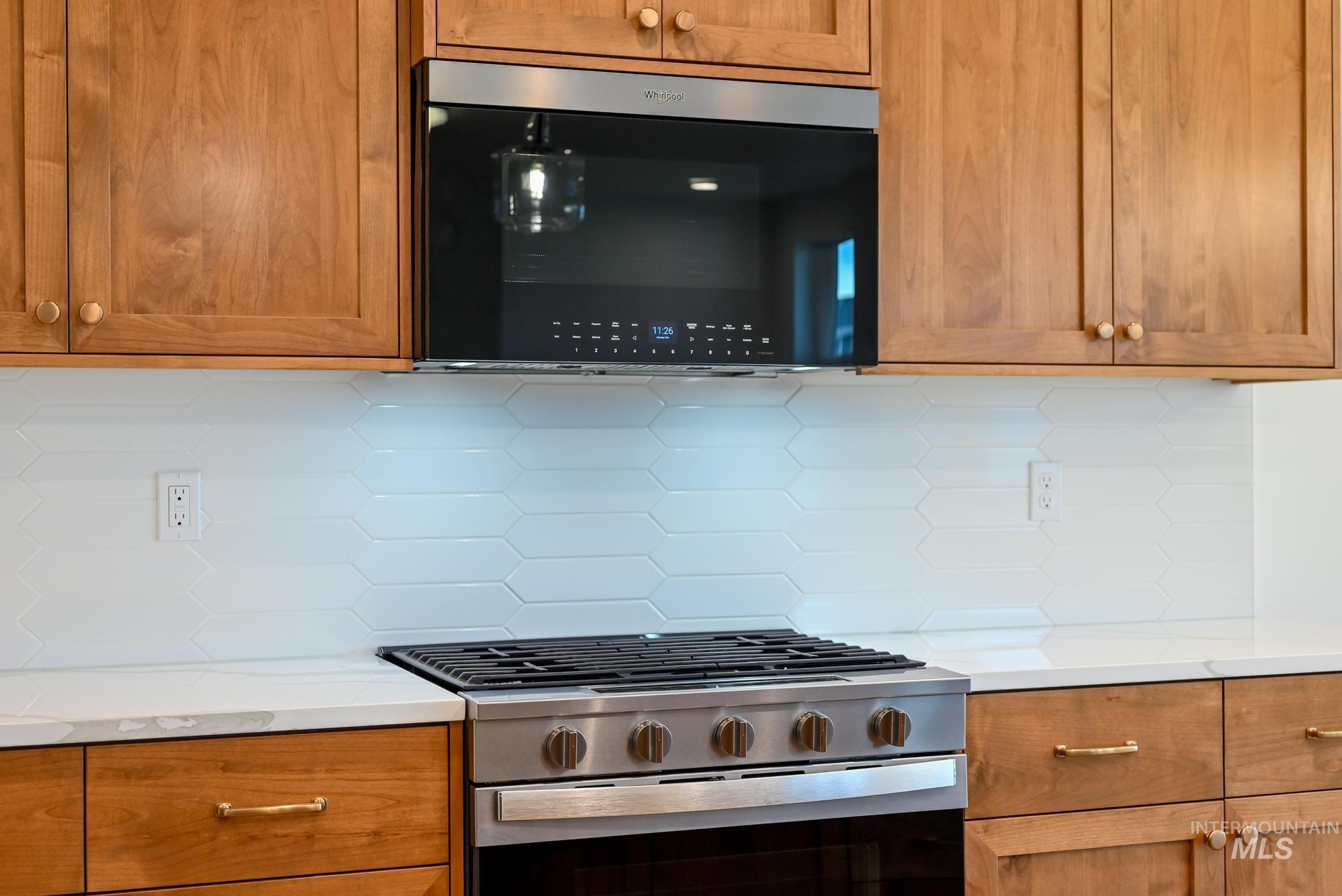Kitchen featuring stainless steel gas stove, brown cabinets, decorative backsplash, and light stone countertops