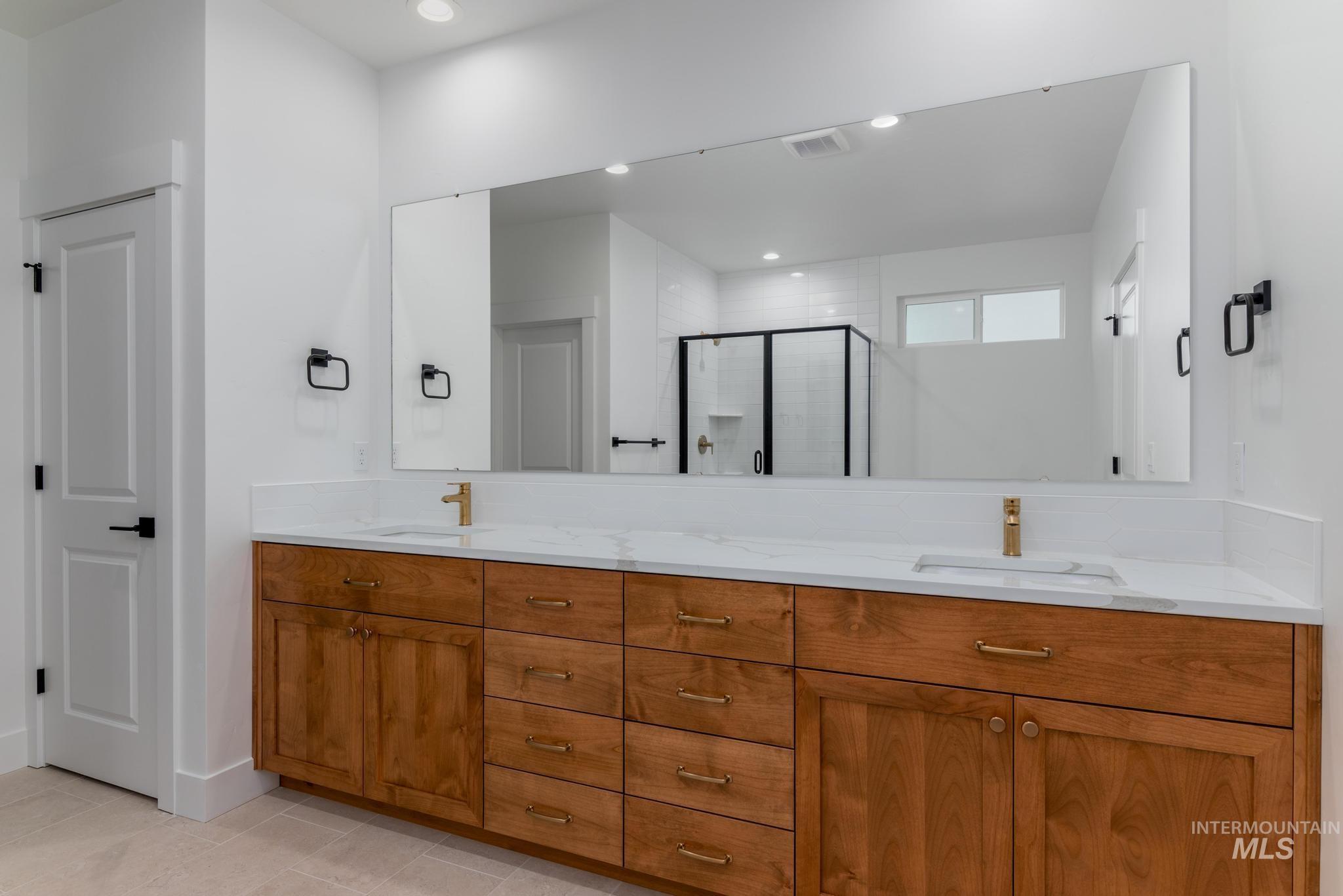 Full bathroom featuring double vanity, a stall shower, recessed lighting, and light tile patterned floors
