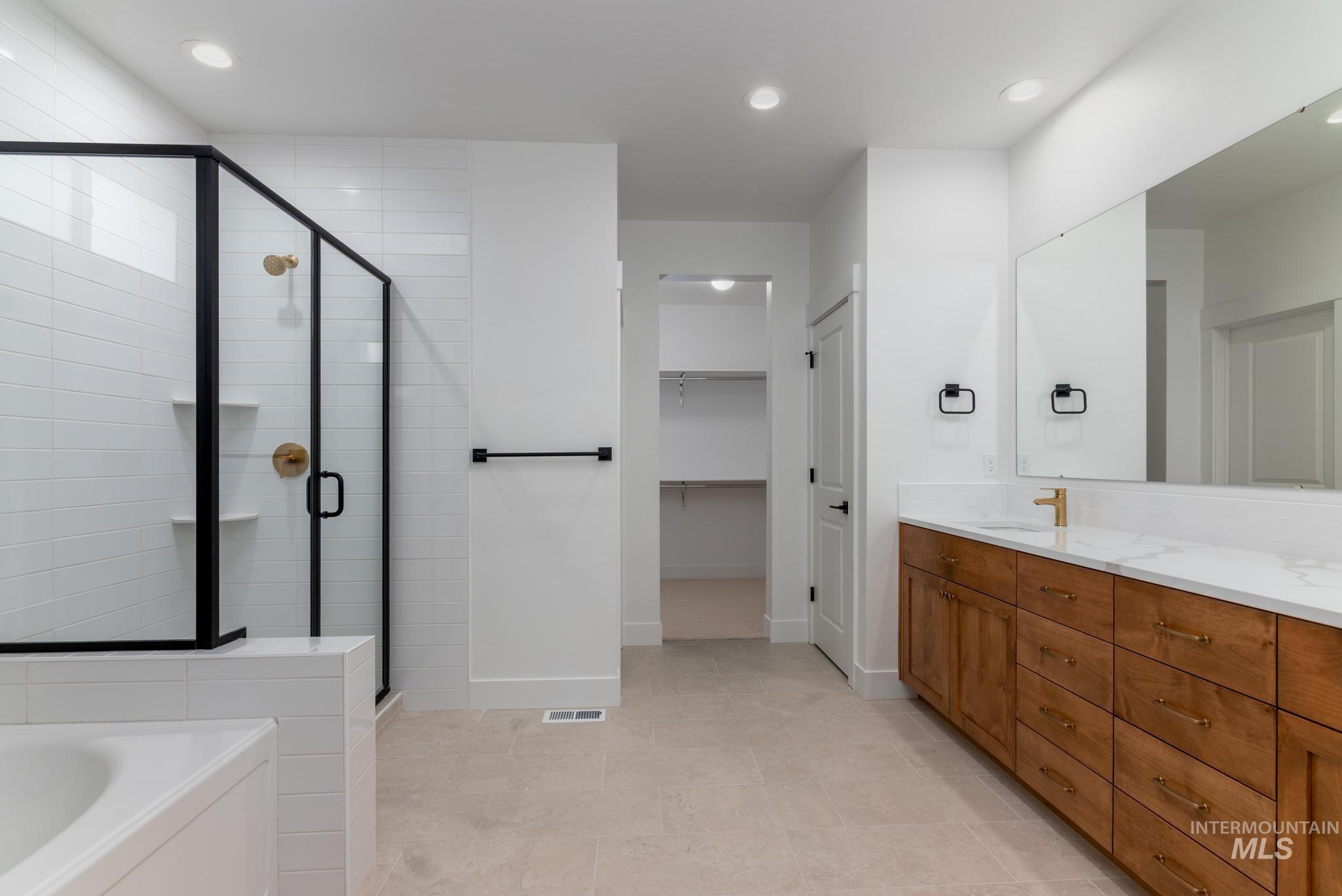 Full bathroom featuring a garden tub, double vanity, a walk in closet, recessed lighting, and a shower stall