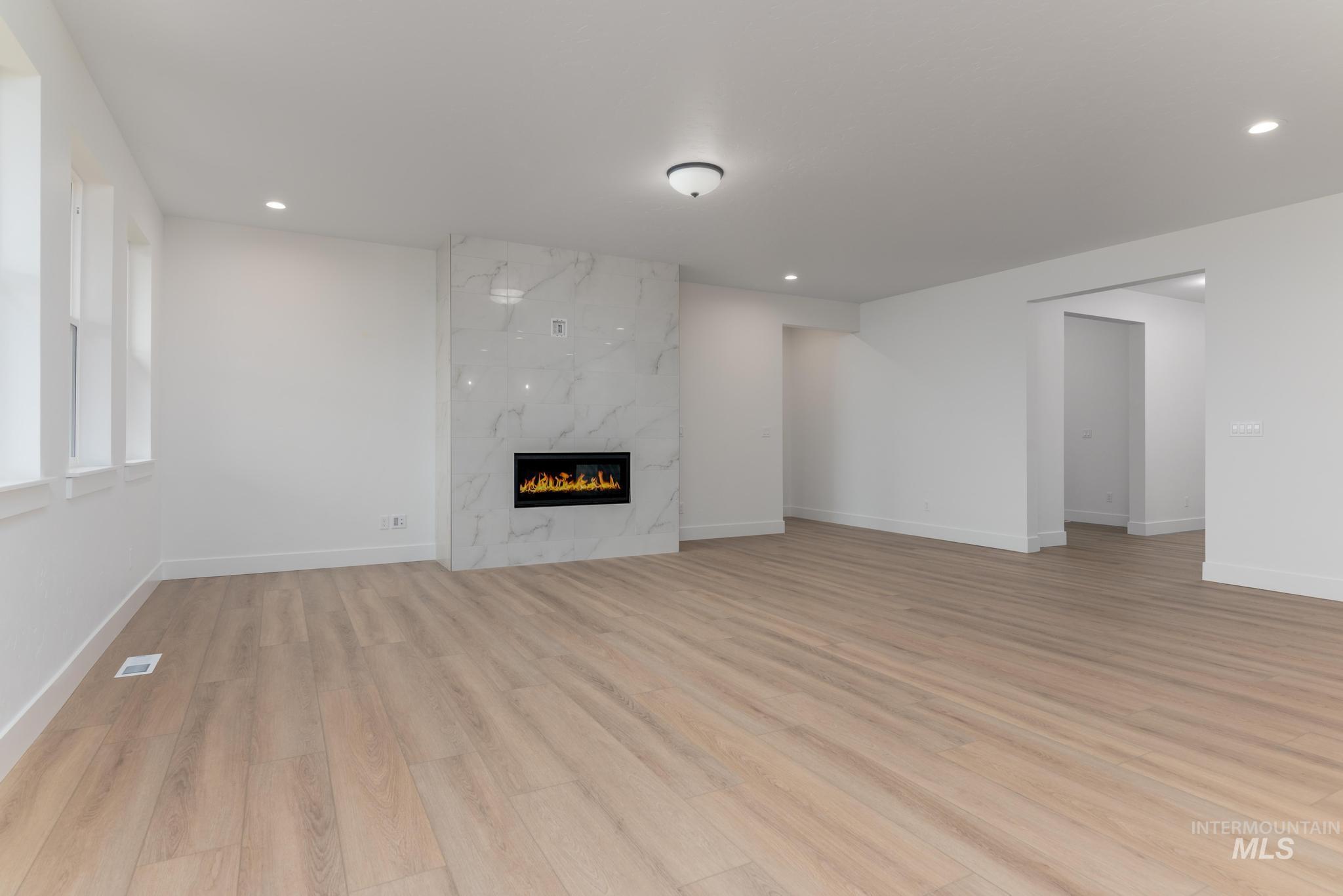 Unfurnished living room with light wood-style floors, a high end fireplace, and recessed lighting