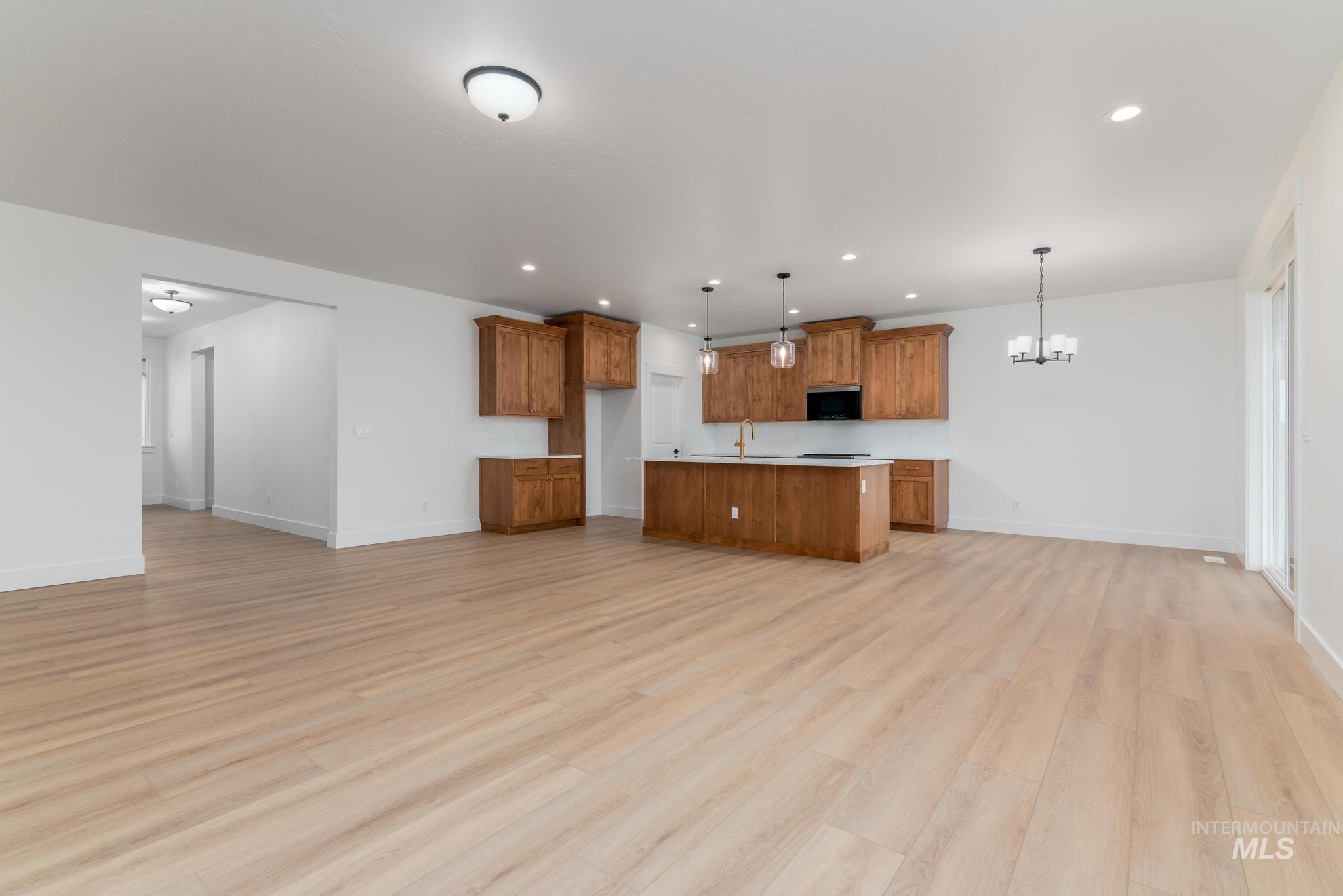 Kitchen with brown cabinets, open floor plan, an island with sink, pendant lighting, and recessed lighting