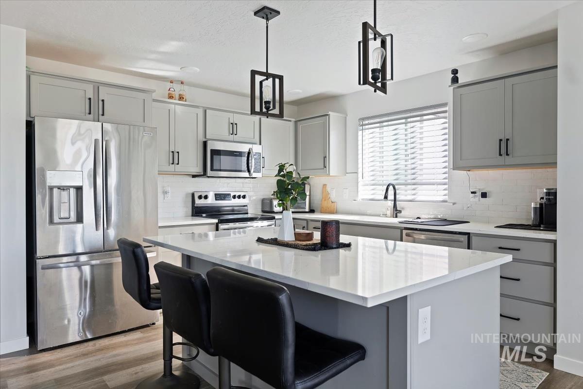 Kitchen featuring gray cabinetry, appliances with stainless steel finishes, hanging light fixtures, a kitchen bar, and light wood-style floors