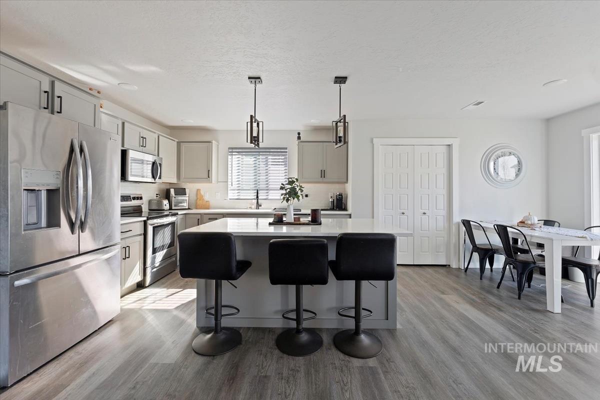 Kitchen featuring appliances with stainless steel finishes, a center island, pendant lighting, a kitchen breakfast bar, and a textured ceiling