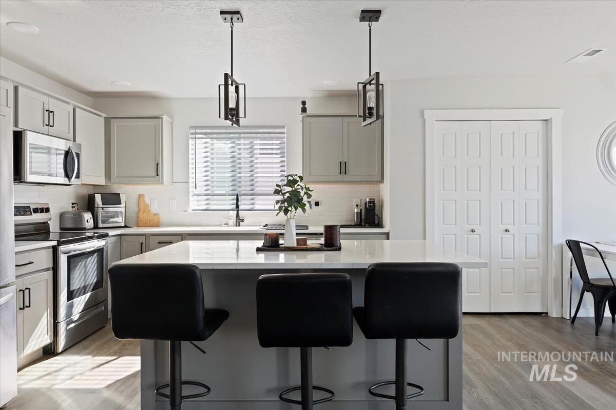 Kitchen with gray cabinets, hanging light fixtures, appliances with stainless steel finishes, a kitchen island, and a textured ceiling