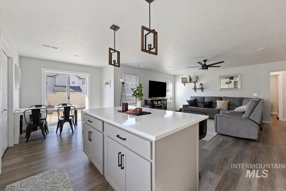 Kitchen featuring hanging light fixtures, a center island, dark wood-style floors, light stone counters, and a textured ceiling
