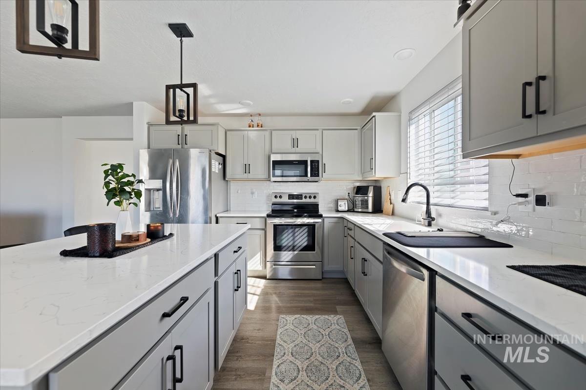 Kitchen featuring gray cabinetry, stainless steel appliances, a kitchen island, light stone counters, and hanging light fixtures