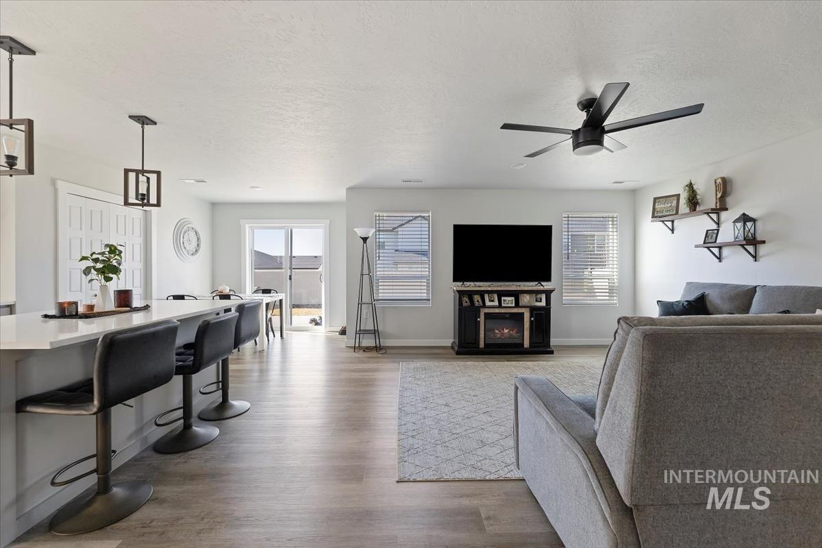 Living room with light wood-style flooring, a textured ceiling, a glass covered fireplace, and ceiling fan
