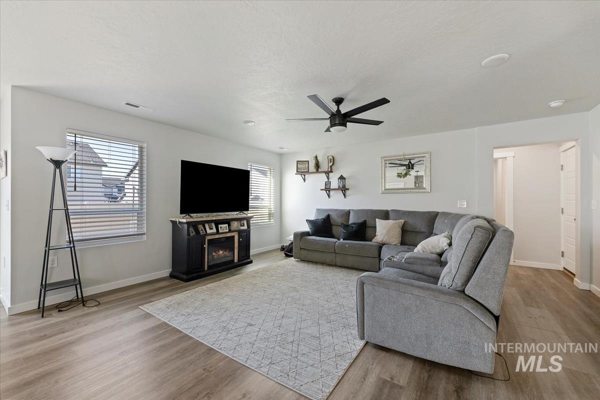 Living area with light wood-type flooring, a lit fireplace, and a ceiling fan