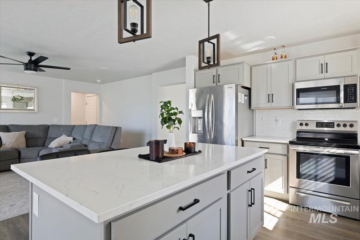 Kitchen featuring stainless steel appliances, a center island, open floor plan, light stone countertops, and light wood-type flooring