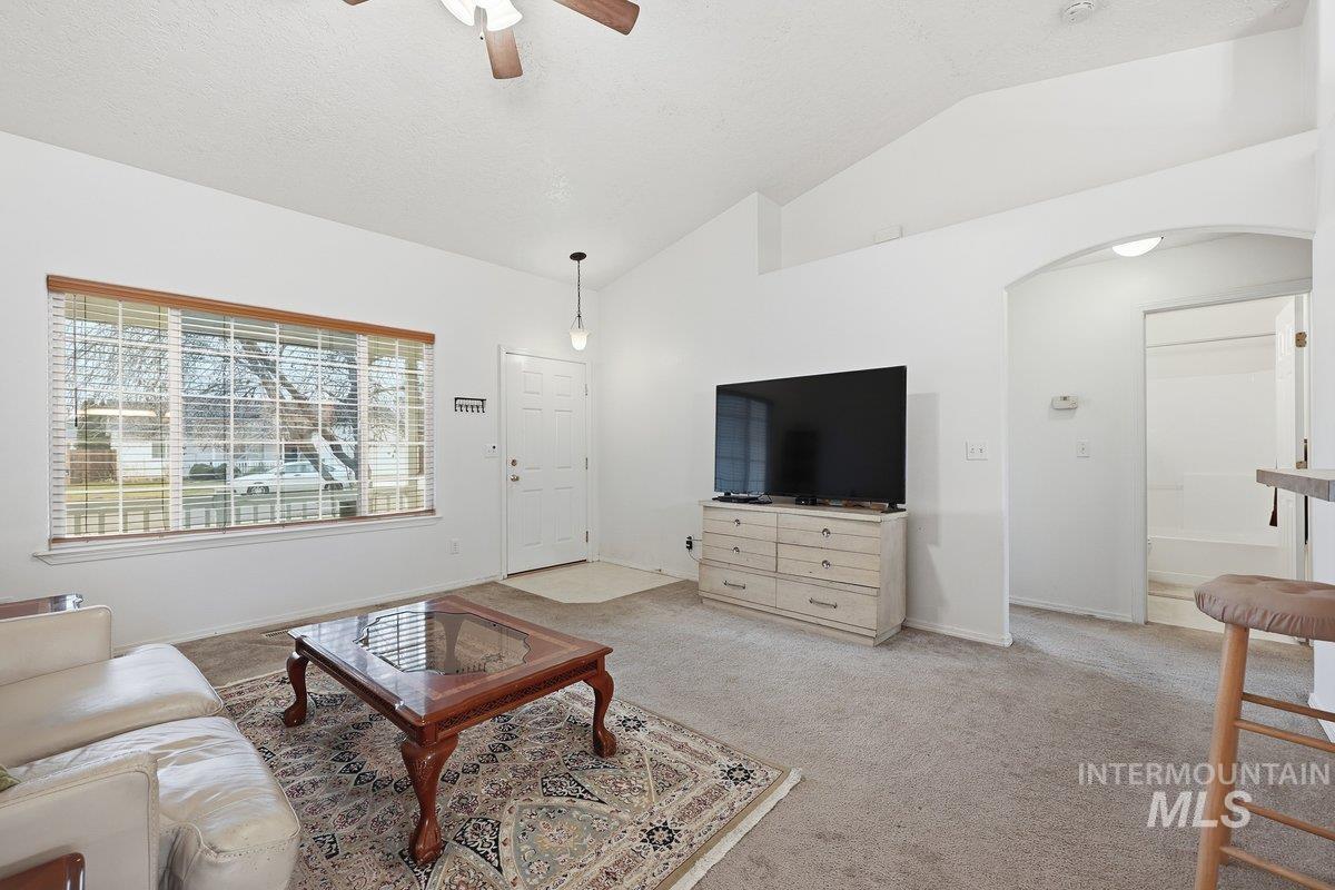 Living room featuring vaulted ceiling, light colored carpet, ceiling fan, and arched walkways