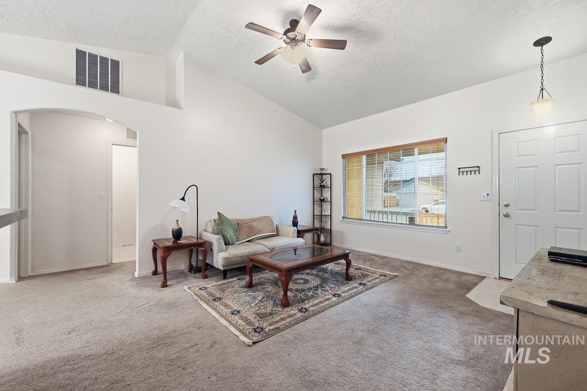 Carpeted living room featuring arched walkways, a ceiling fan, a textured ceiling, and high vaulted ceiling