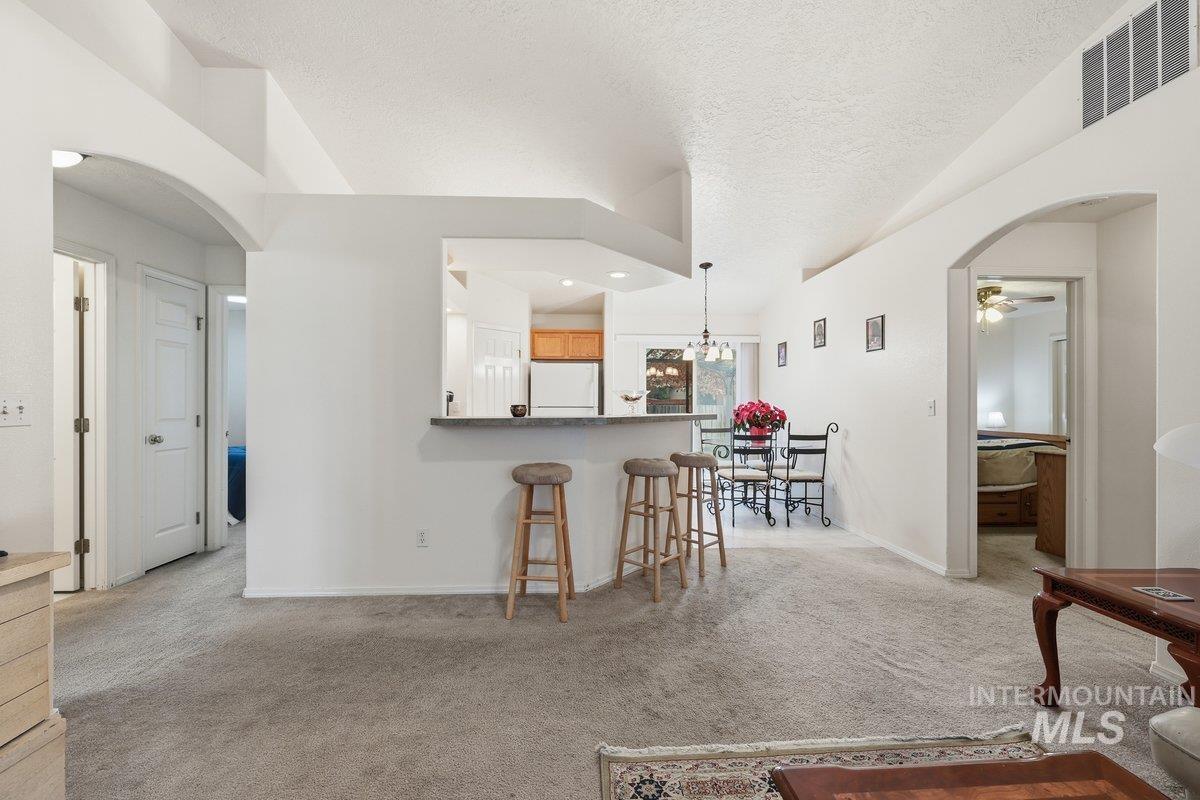Living area with arched walkways, light carpet, a ceiling fan, and a textured ceiling