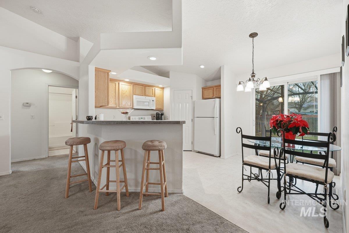 Kitchen with arched walkways, a peninsula, a breakfast bar area, white appliances, and light colored carpet