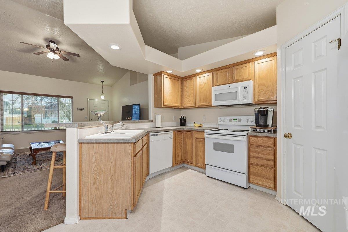 Kitchen featuring white appliances, lofted ceiling, a peninsula, a textured ceiling, and light countertops