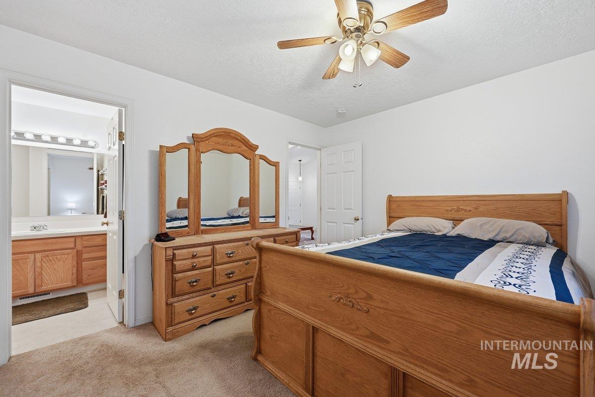 Bedroom with light colored carpet, a ceiling fan, ensuite bathroom, and a textured ceiling