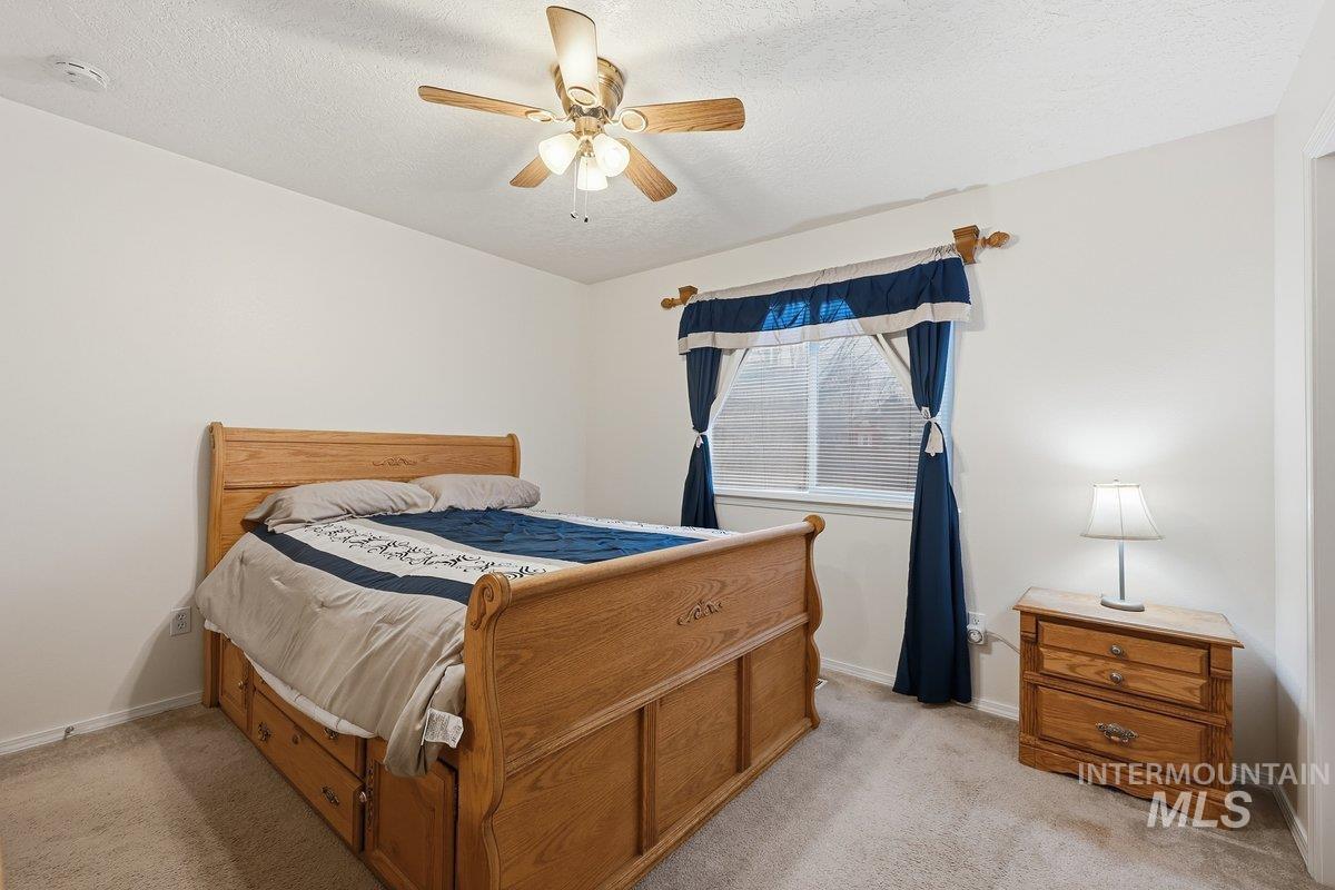 Bedroom with ceiling fan, light carpet, and a textured ceiling
