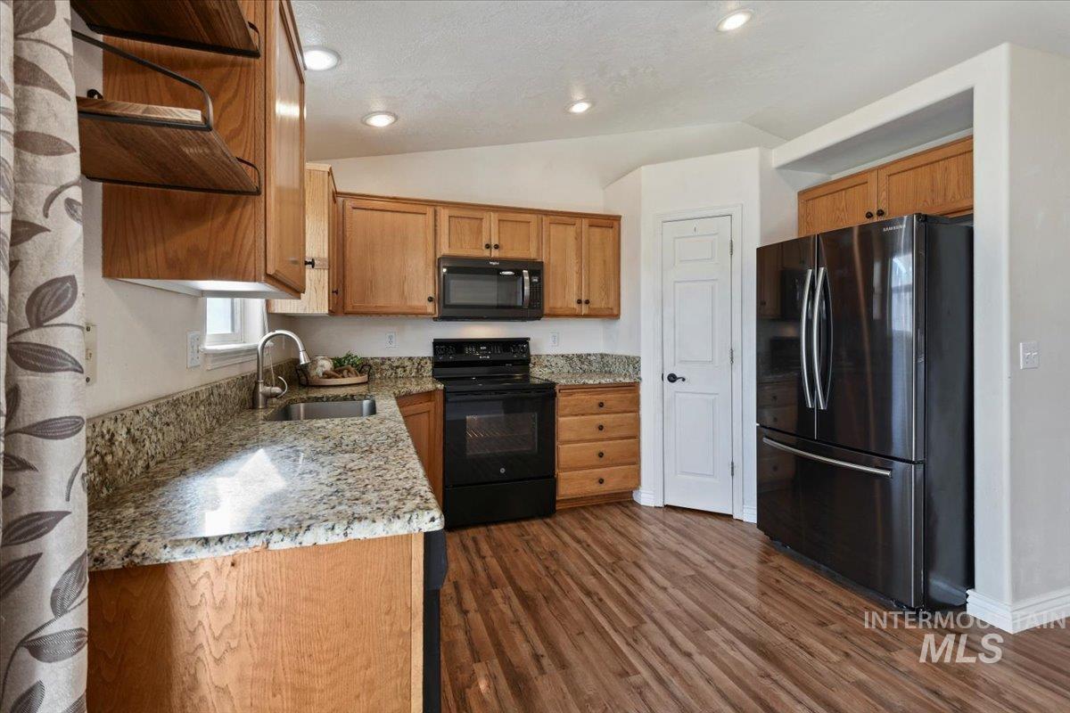 Kitchen with open shelves, lofted ceiling, black appliances, light stone counters, and dark wood-style flooring