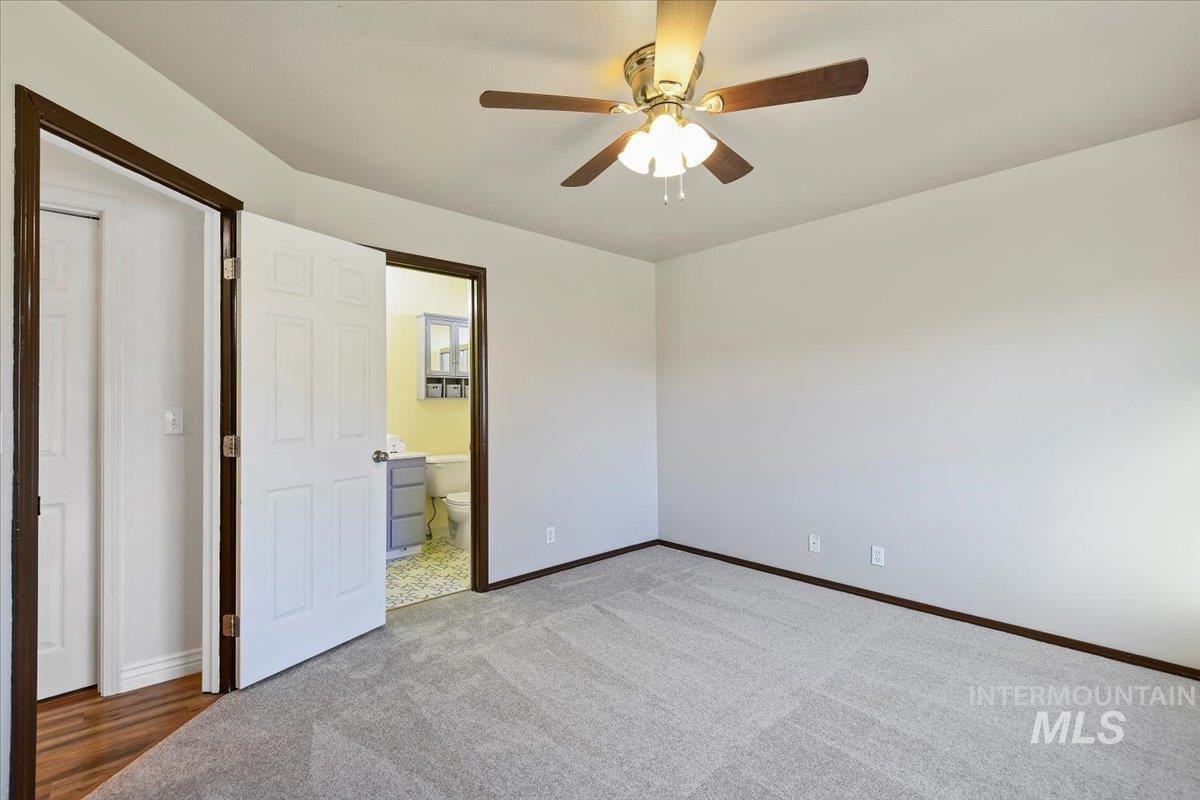 Unfurnished bedroom featuring carpet, ensuite bathroom, and ceiling fan
