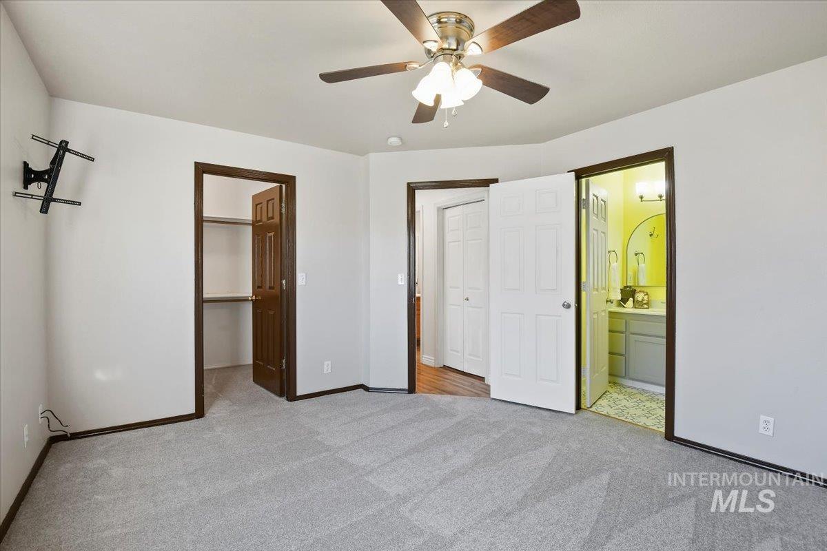 Unfurnished bedroom with a spacious closet, a ceiling fan, light colored carpet, and ensuite bathroom