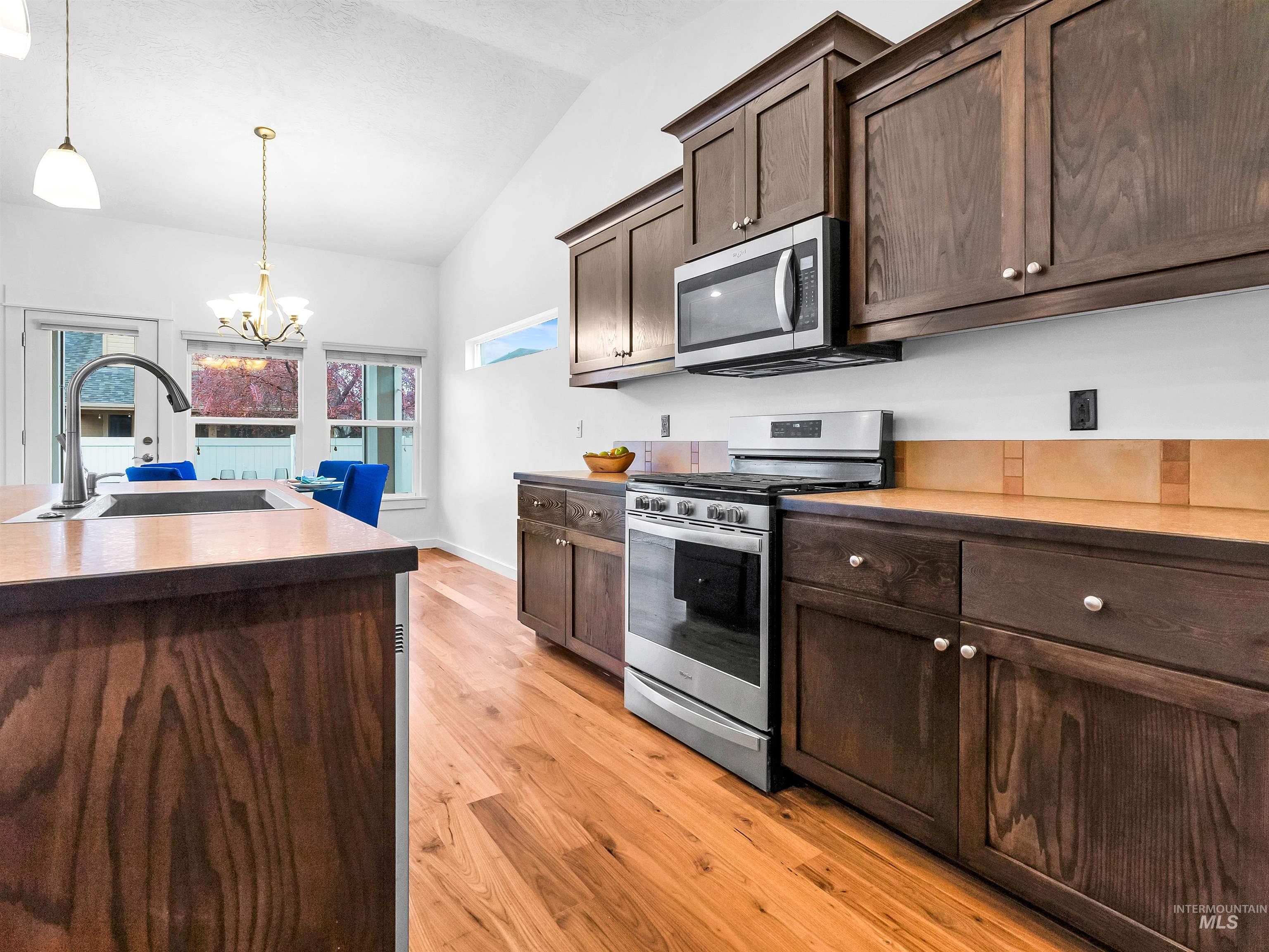 Kitchen featuring dark brown cabinets, appliances with stainless steel finishes, vaulted ceiling, a chandelier, and pendant lighting