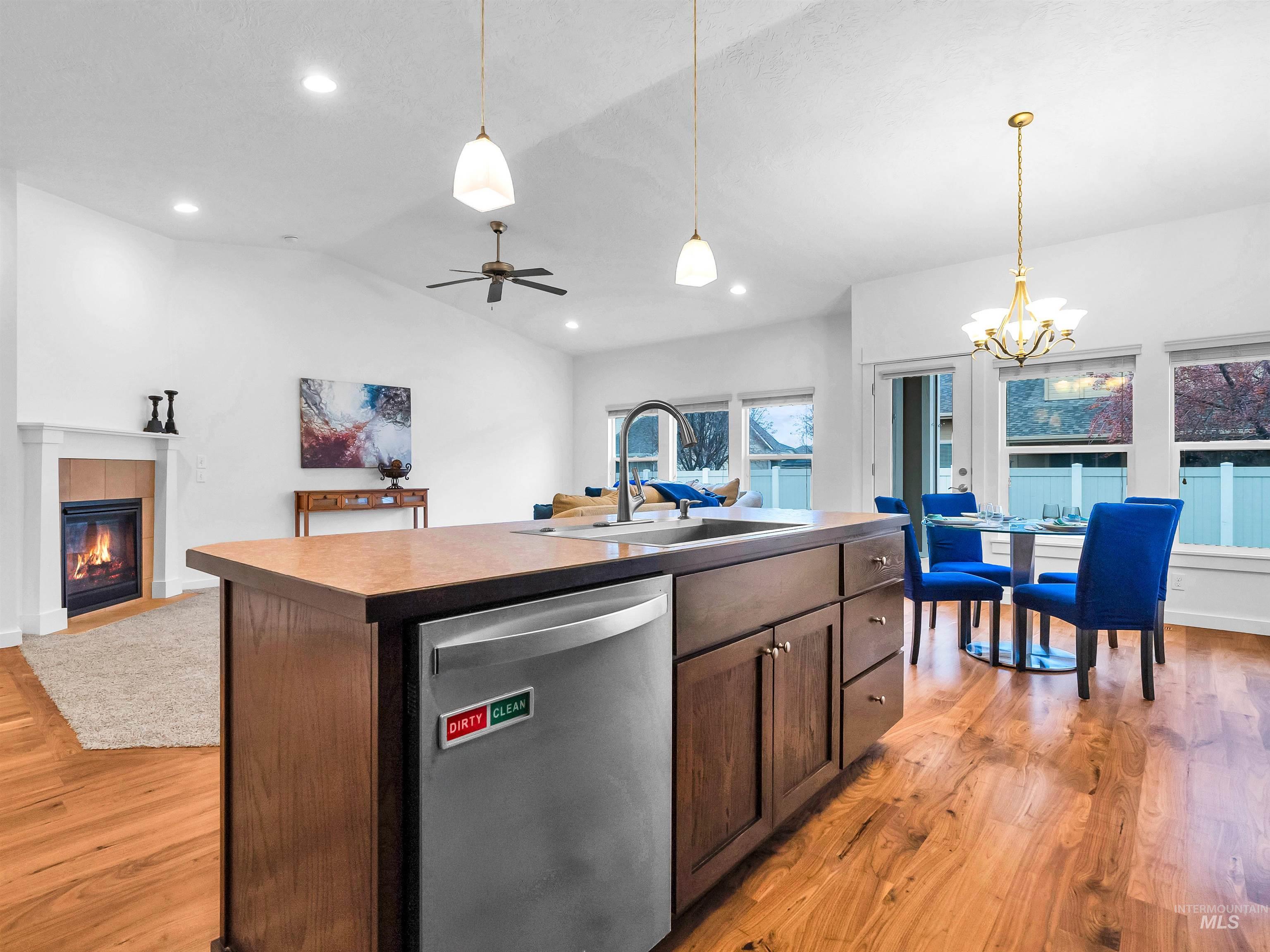 Kitchen with open floor plan, stainless steel dishwasher, a center island with sink, vaulted ceiling, and dark brown cabinetry