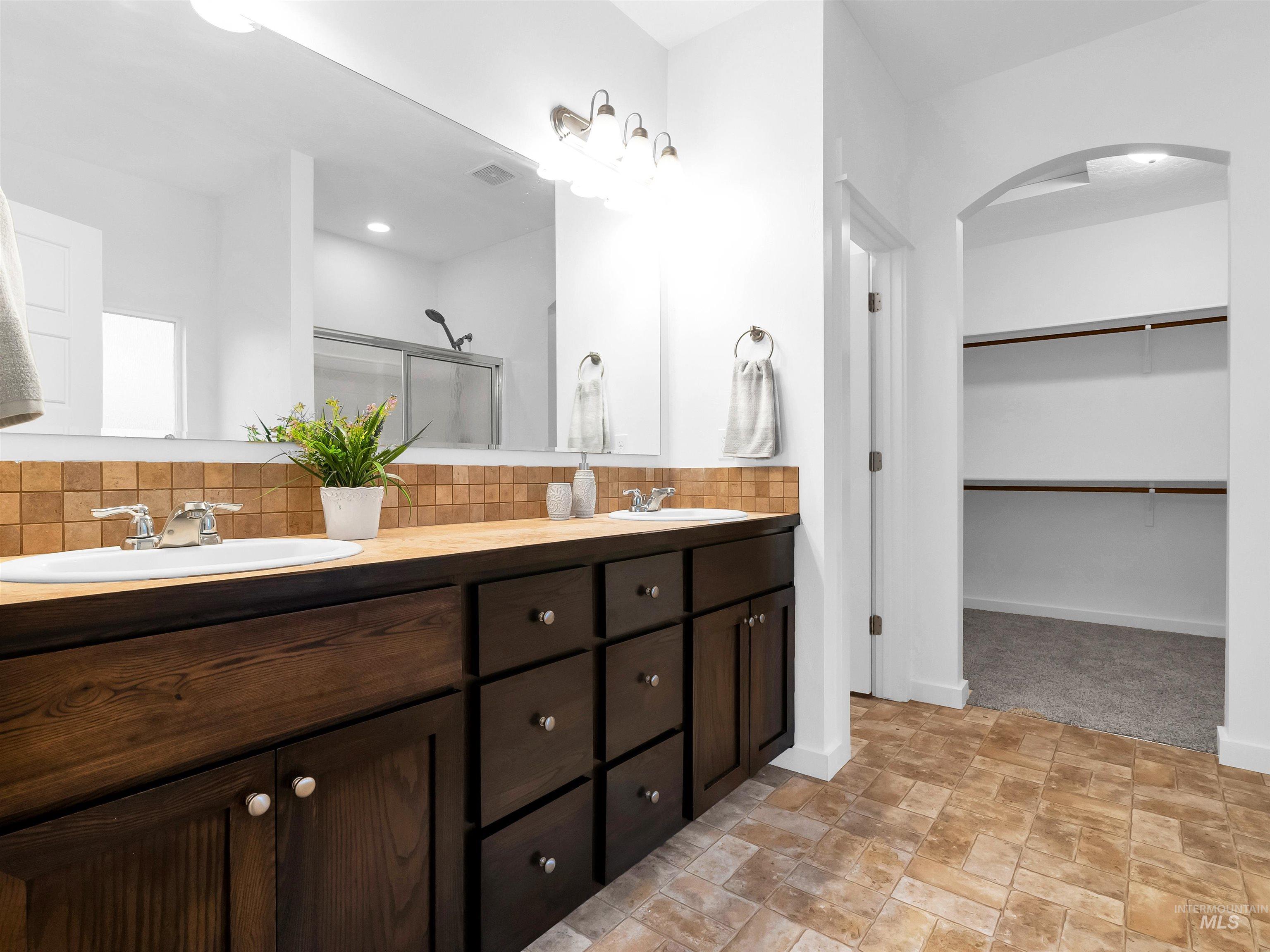 Full bathroom featuring double vanity, backsplash, a stall shower, a spacious closet, and stone finish floors