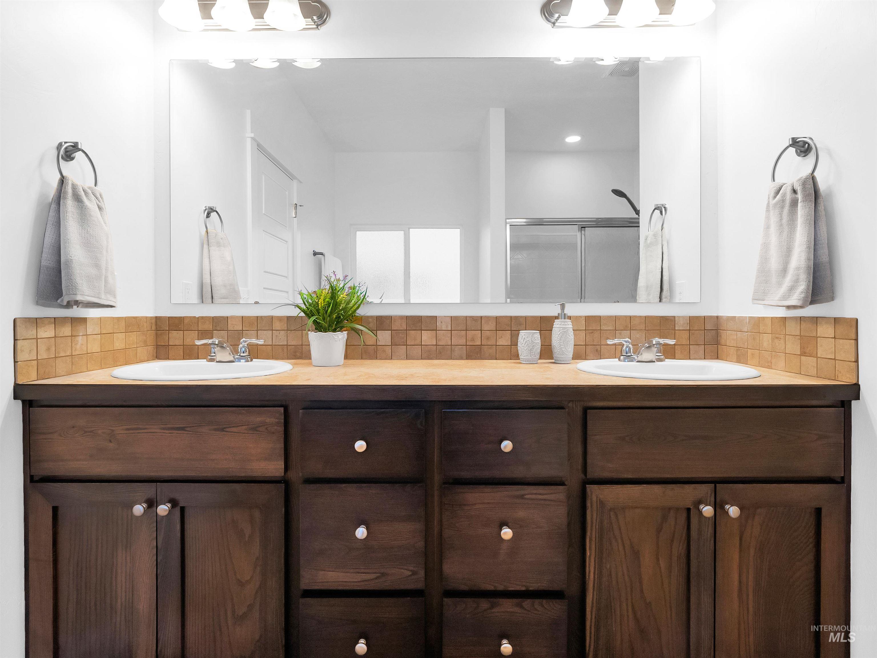 Full bath with backsplash, double vanity, and a shower stall
