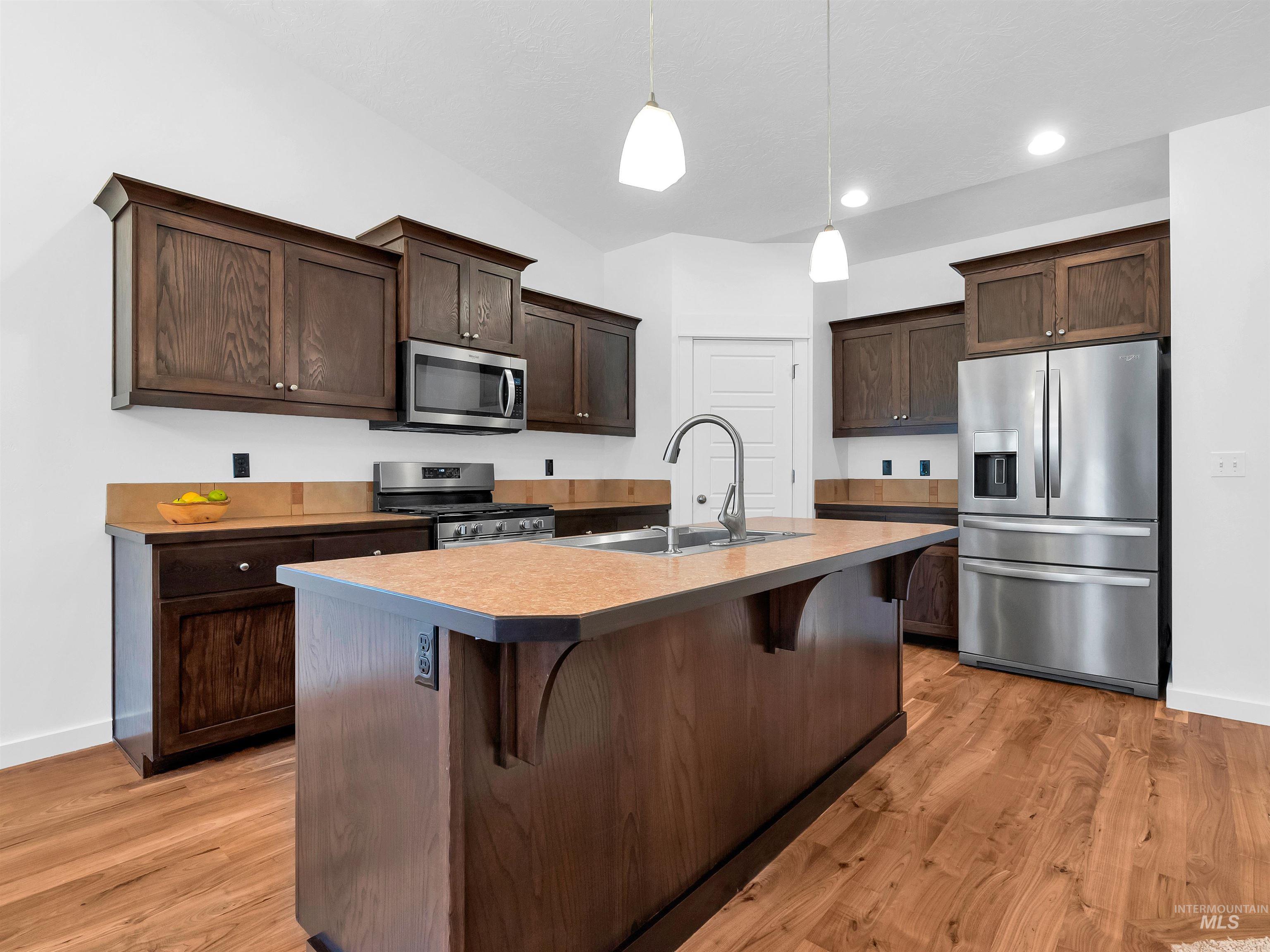 Kitchen featuring a breakfast bar, appliances with stainless steel finishes, dark brown cabinetry, hanging light fixtures, and recessed lighting