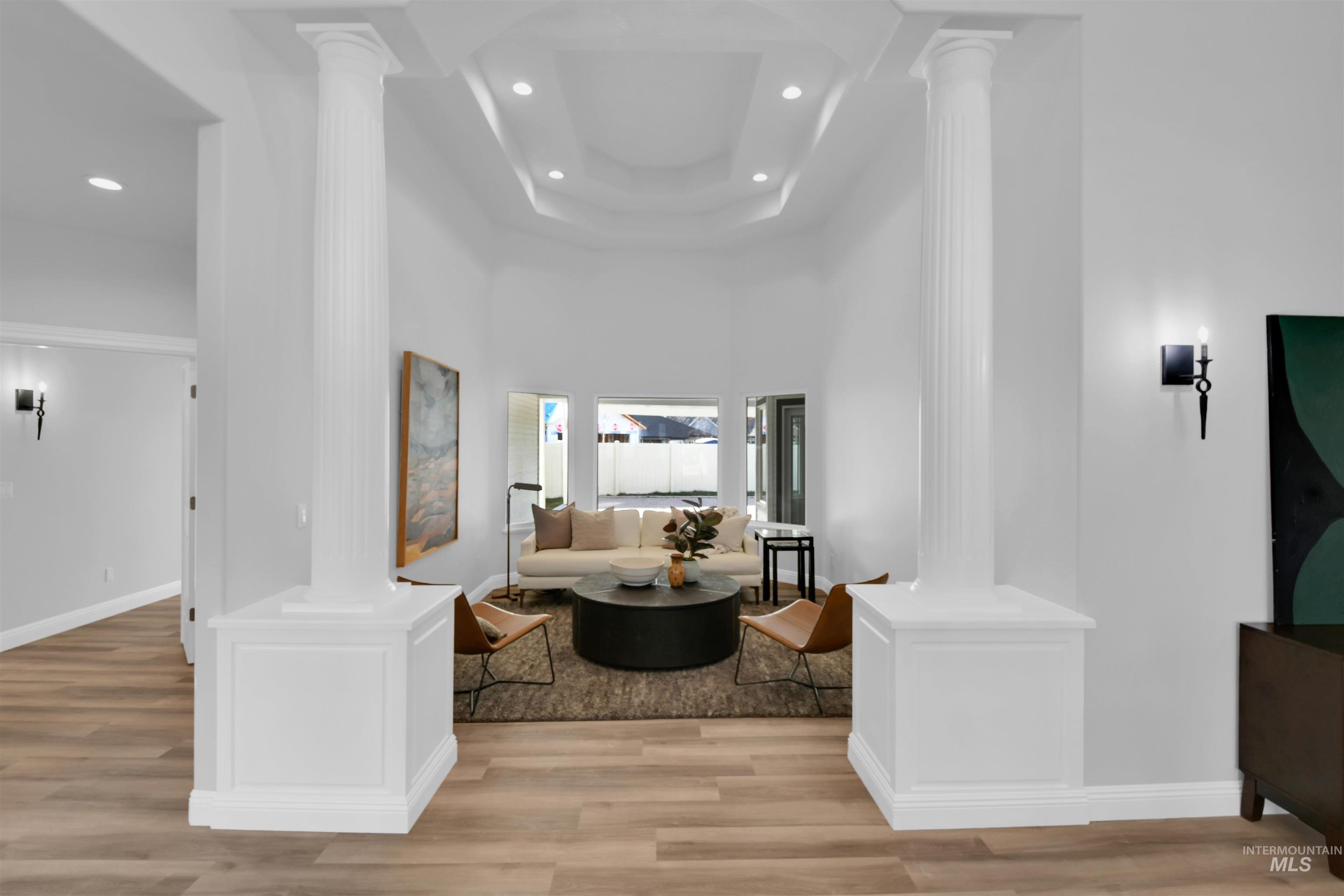 Hall with decorative columns, a towering ceiling, light wood finished floors, and recessed lighting