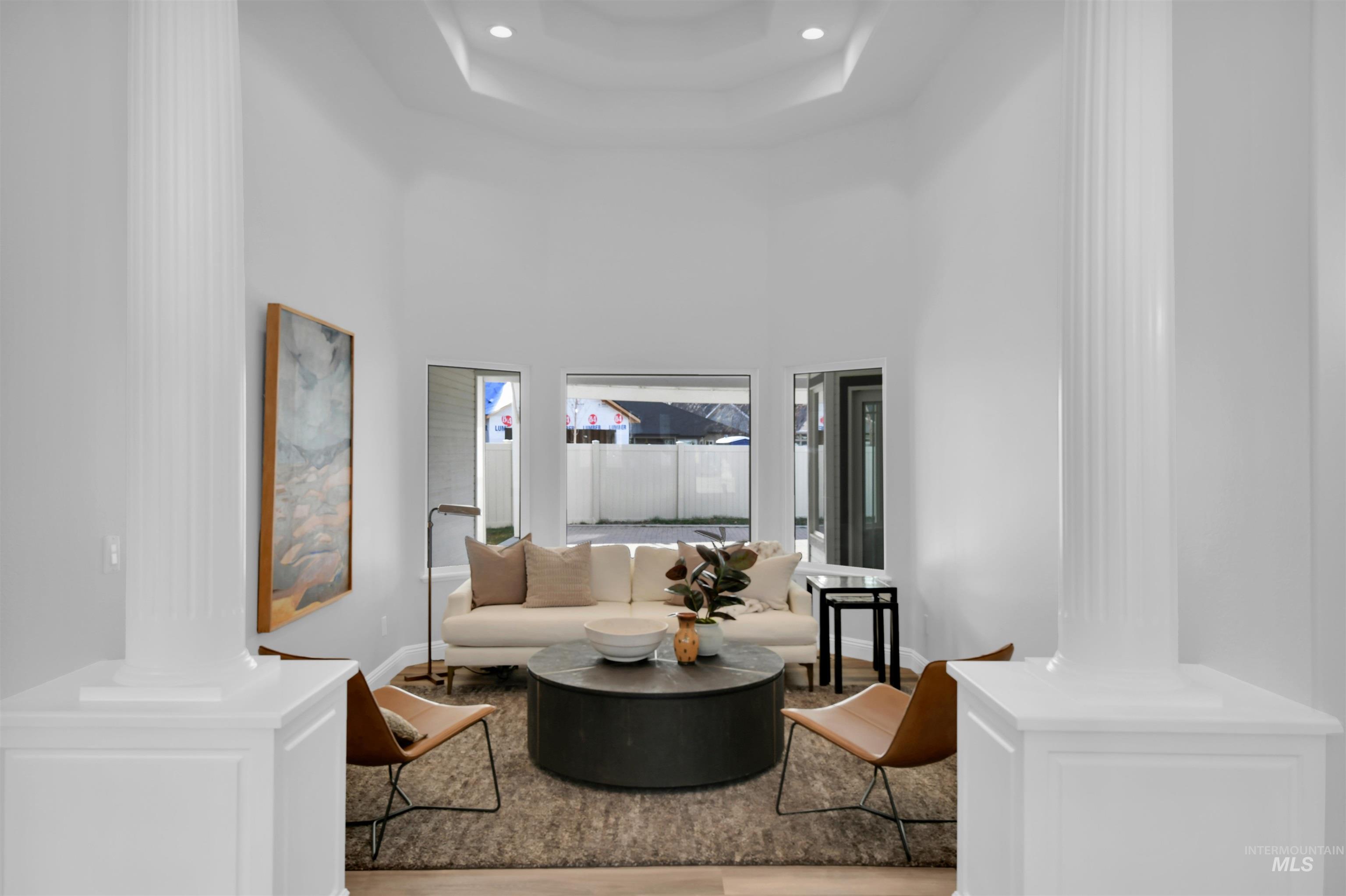 Living area with a towering ceiling, ornate columns, a raised ceiling, recessed lighting, and wood finished floors