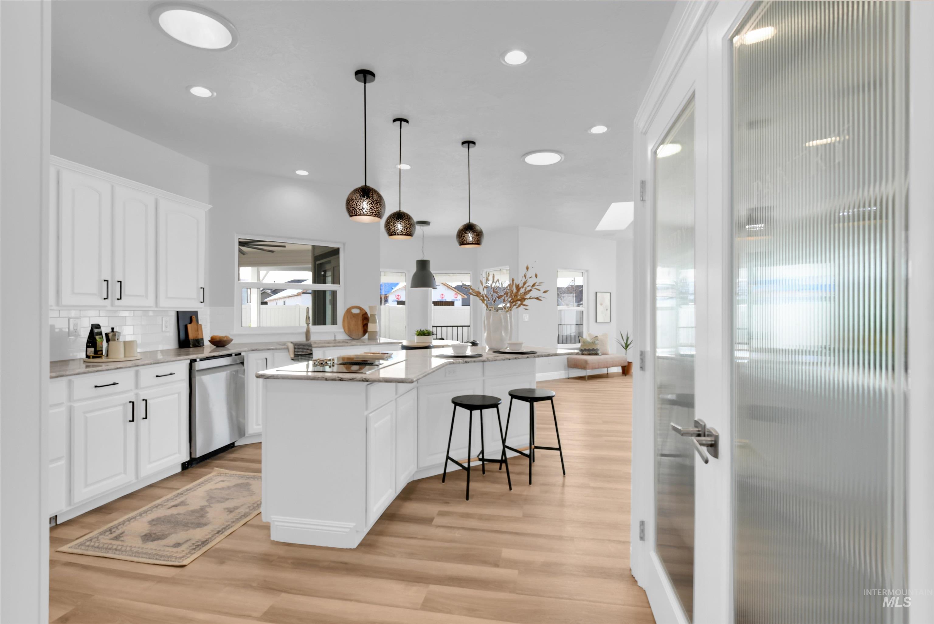Kitchen featuring light stone countertops, white cabinets, hanging light fixtures, a center island, and tasteful backsplash
