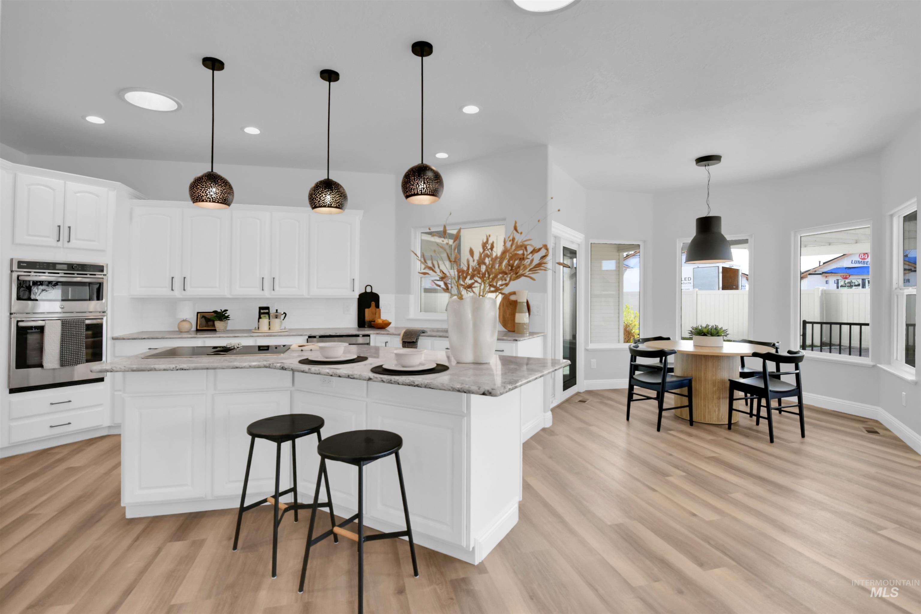 Kitchen featuring light stone countertops, white cabinets, decorative light fixtures, stainless steel double oven, and a kitchen island