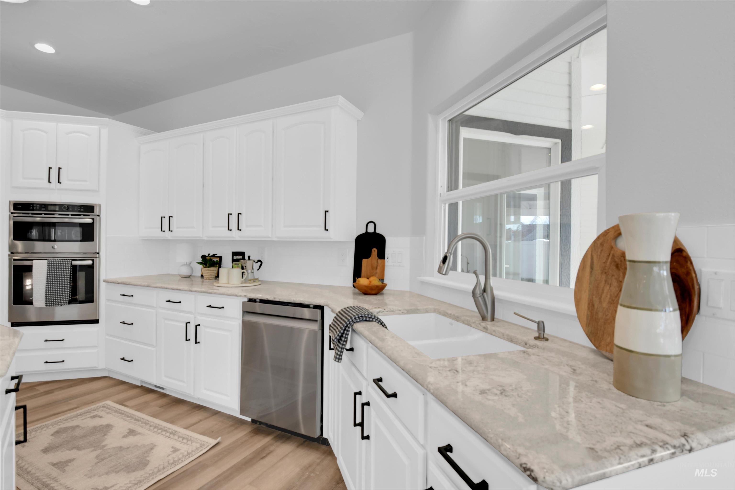 Kitchen with stainless steel appliances, white cabinets, light stone countertops, light wood-style flooring, and recessed lighting