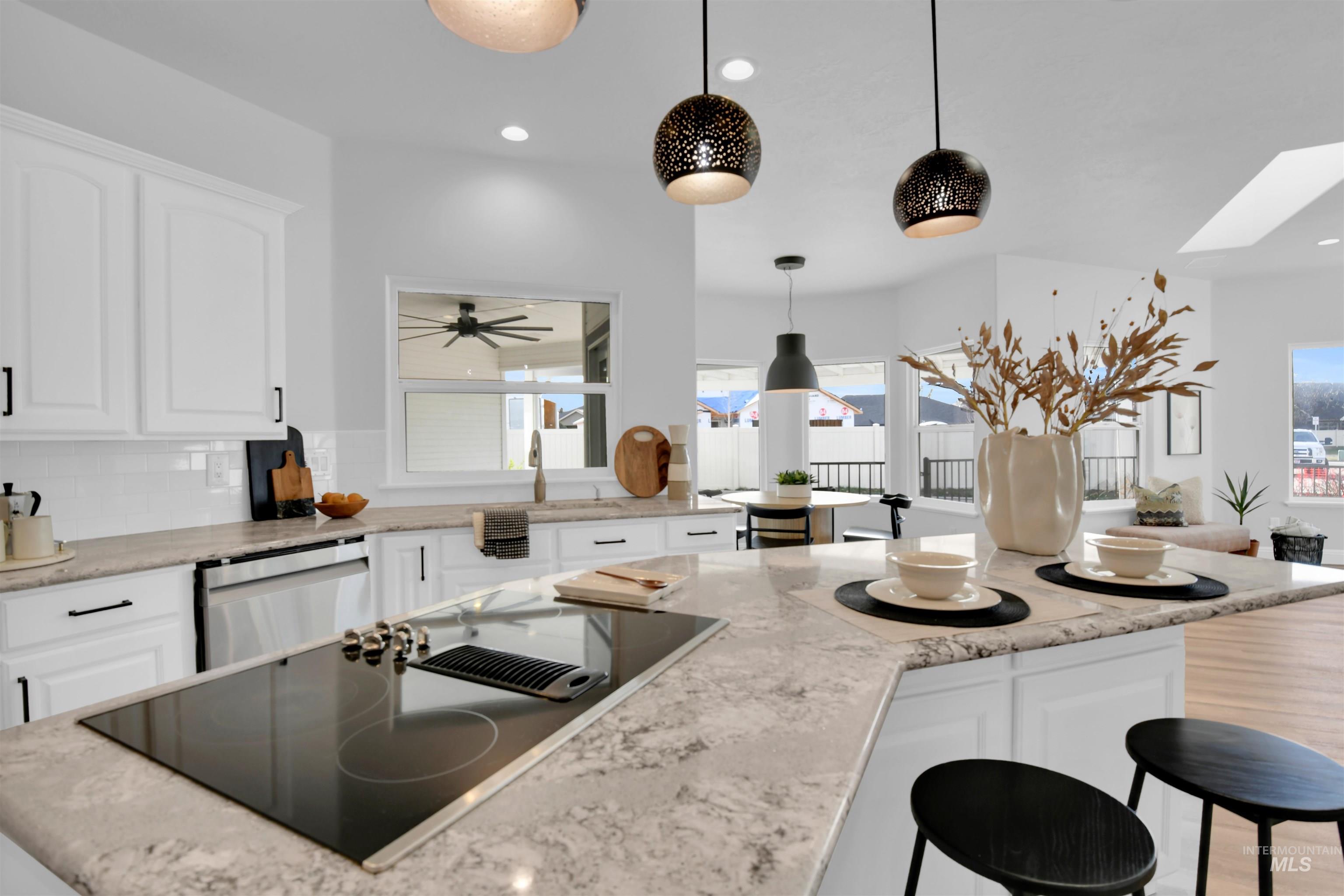 Kitchen featuring white cabinets, black electric cooktop, backsplash, a breakfast bar, and light stone counters