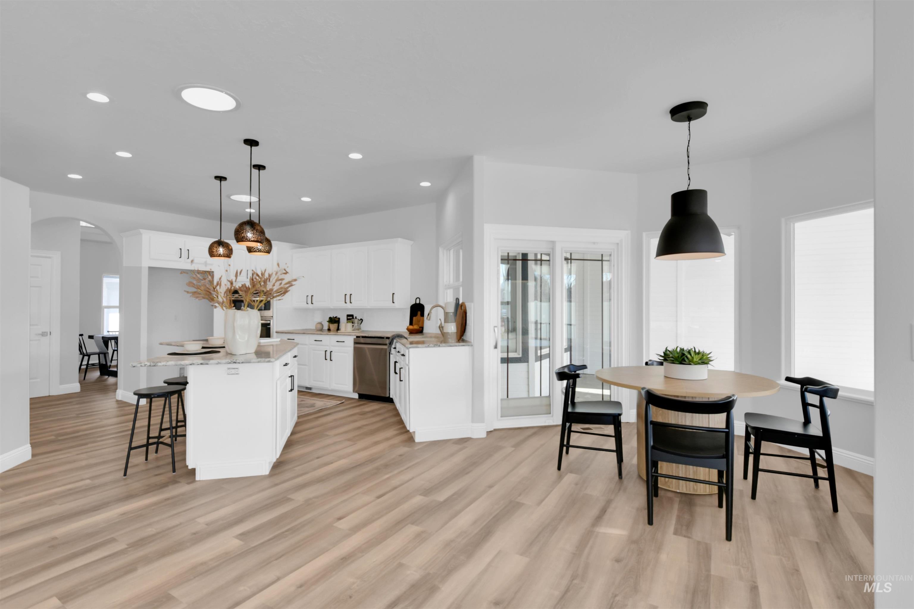 Kitchen with white cabinets, light stone counters, a kitchen bar, arched walkways, and plenty of natural light
