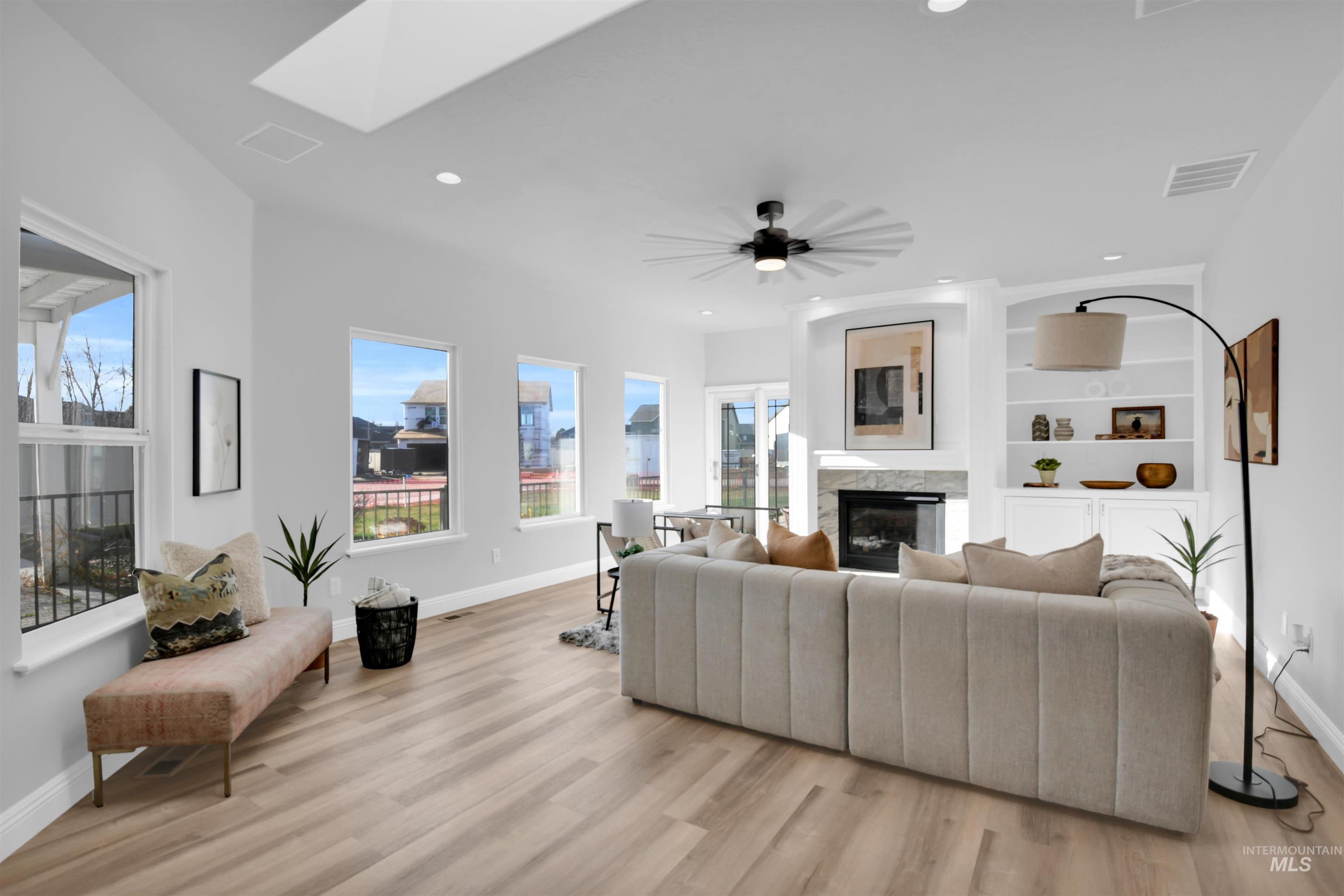Living area featuring a high end fireplace, a skylight, healthy amount of natural light, light wood-type flooring, and recessed lighting