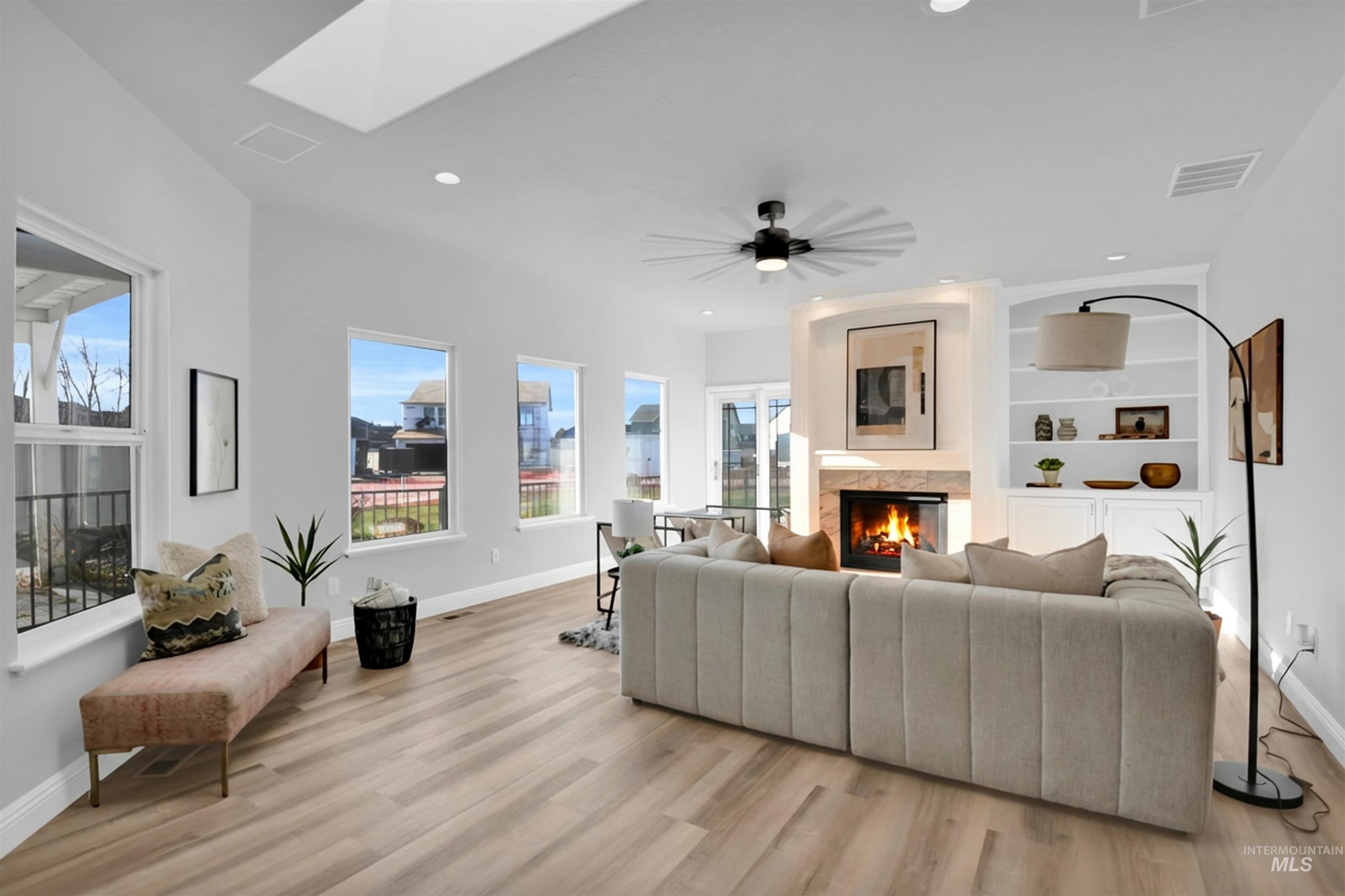 Living area featuring a lit fireplace, a skylight, light wood-style floors, built in shelves, and recessed lighting