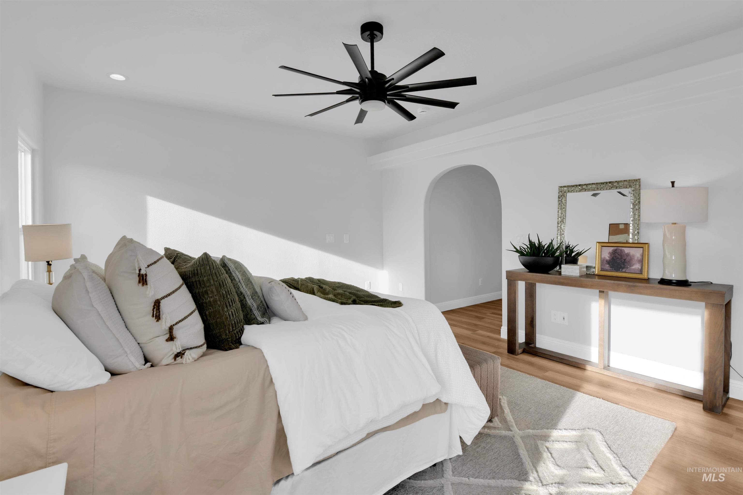 Bedroom with arched walkways, light wood-type flooring, ceiling fan, and recessed lighting