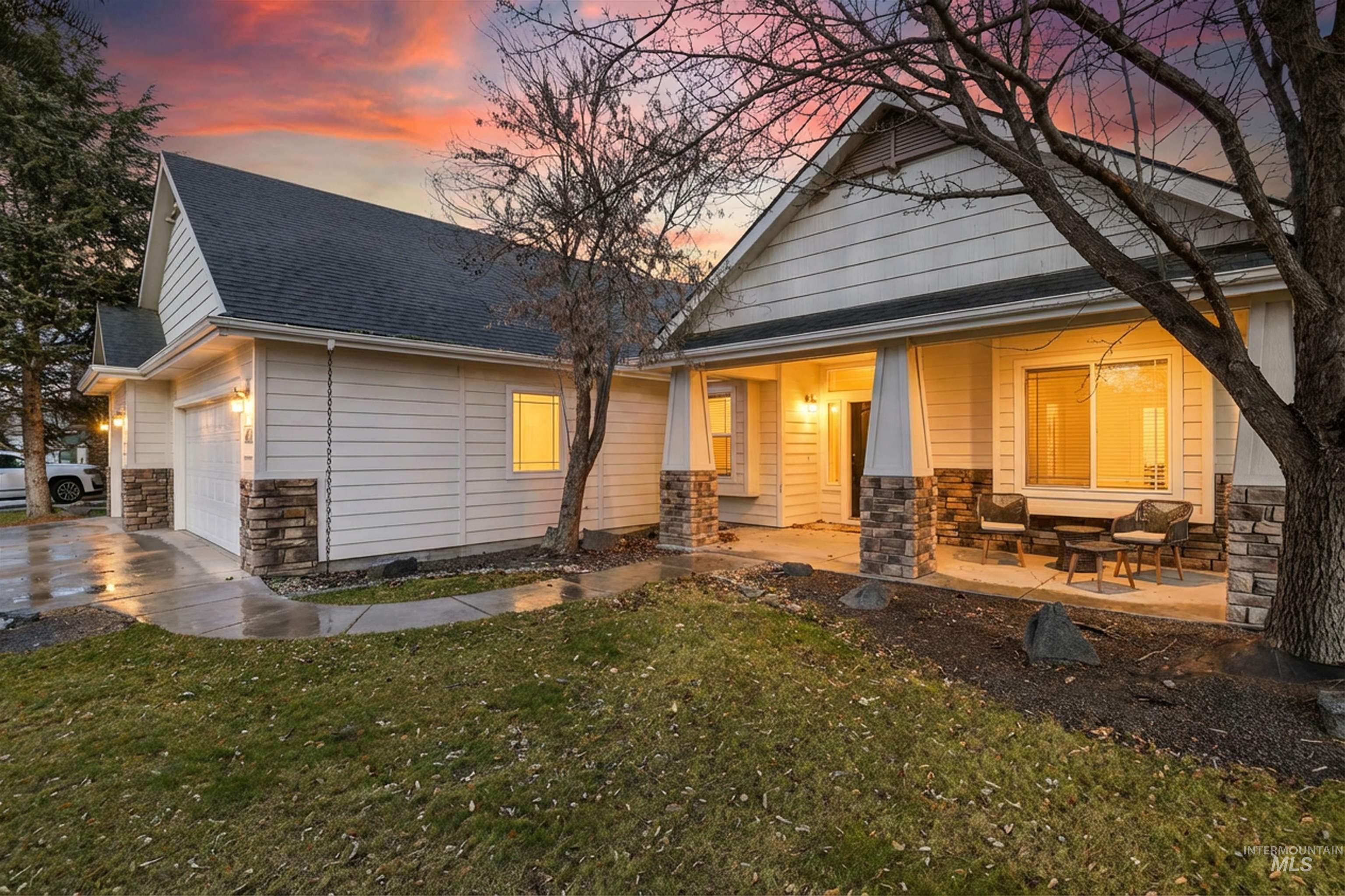 Back of house at dusk featuring stone siding, a shingled roof, a yard, and concrete driveway