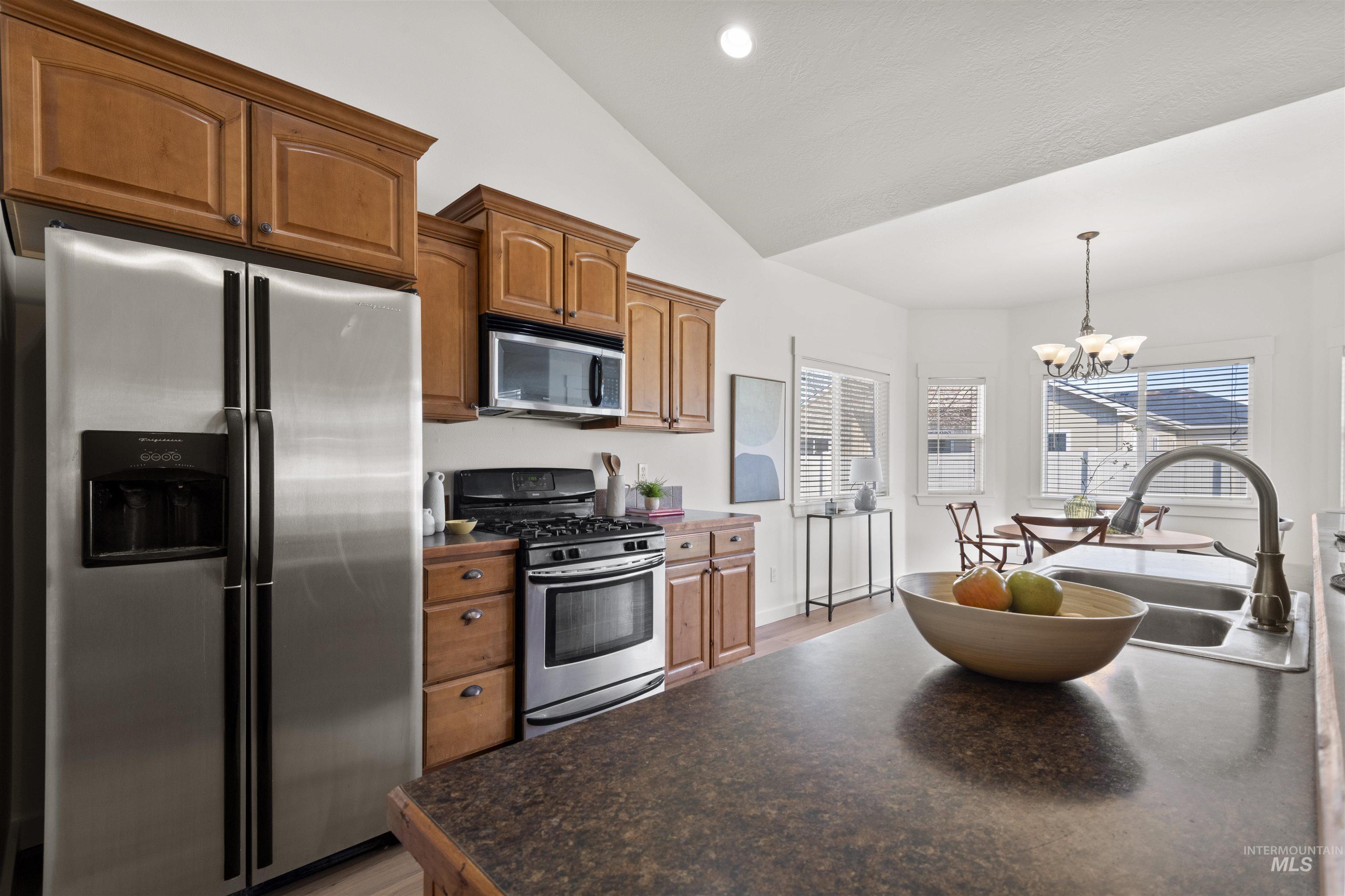 Kitchen with stainless steel appliances, hanging light fixtures, lofted ceiling, a chandelier, and brown cabinets