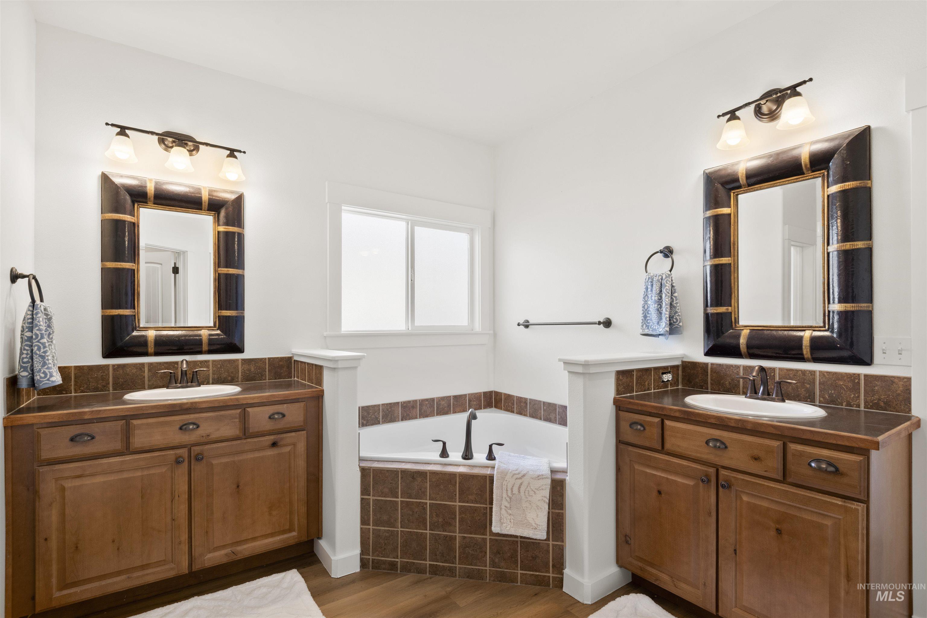 Full bathroom with two vanities, a bath, and dark wood-type flooring