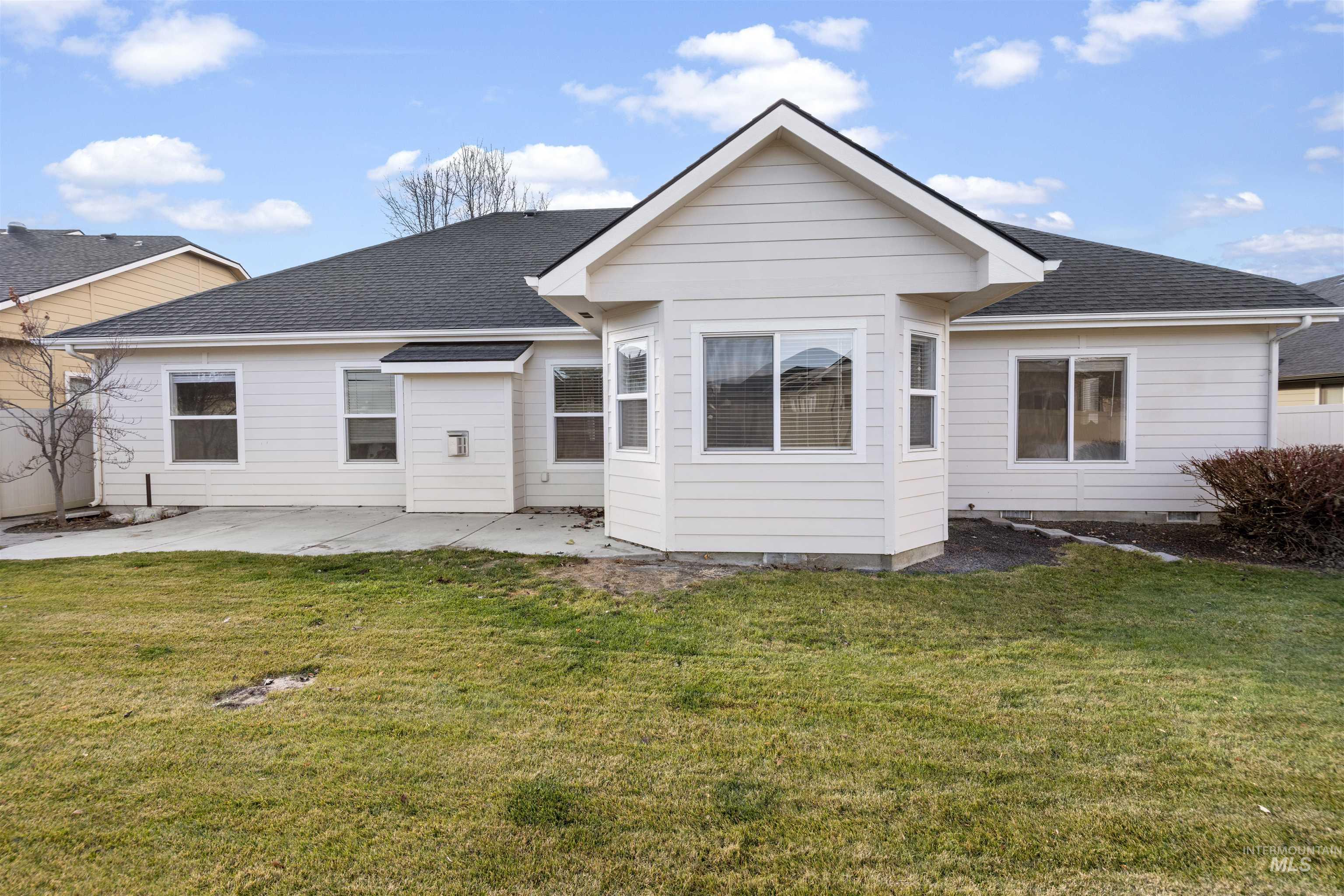 Back of house featuring roof with shingles, a lawn, and a patio