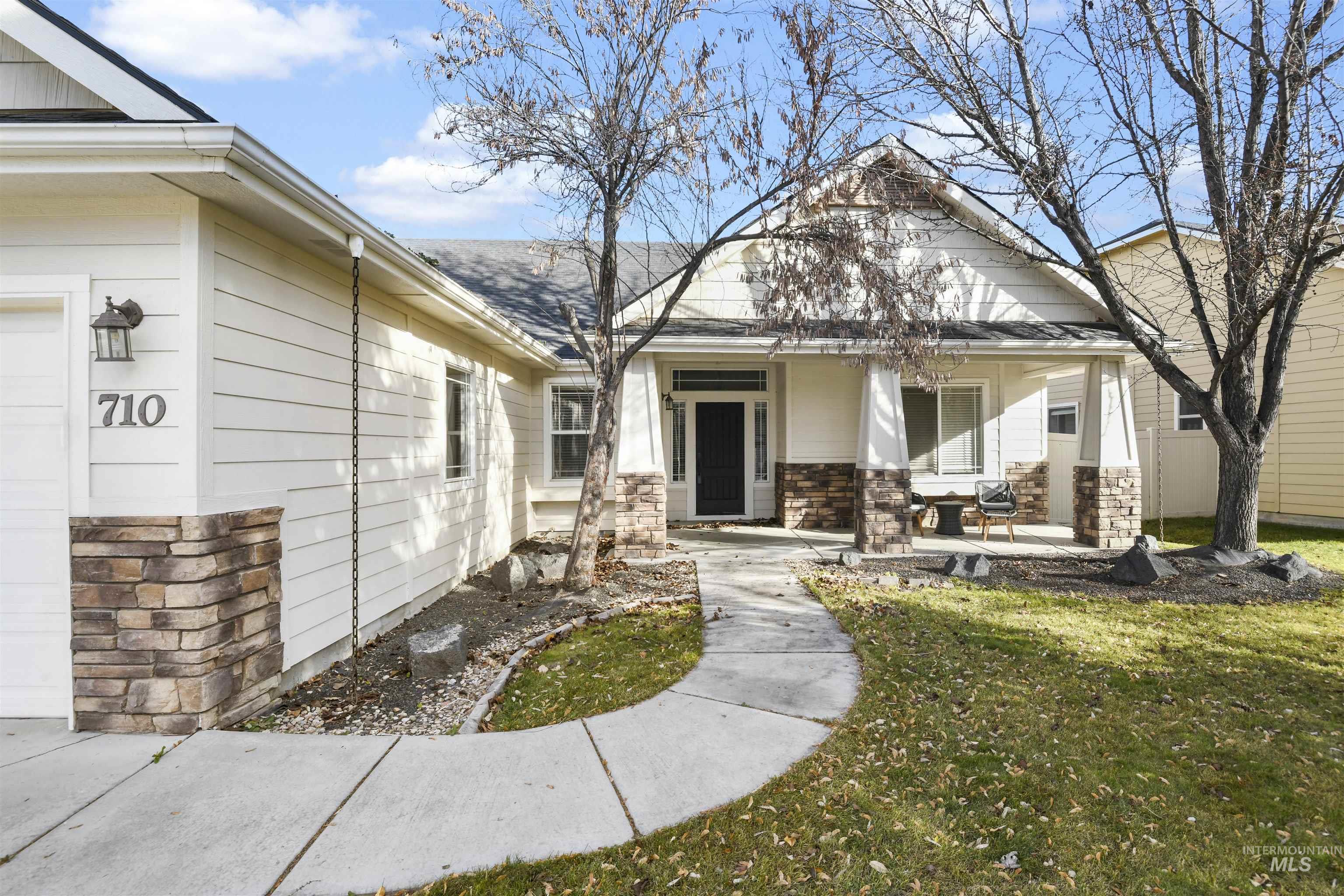 View of front of home with covered porch, stone siding, a front lawn, and a shingled roof