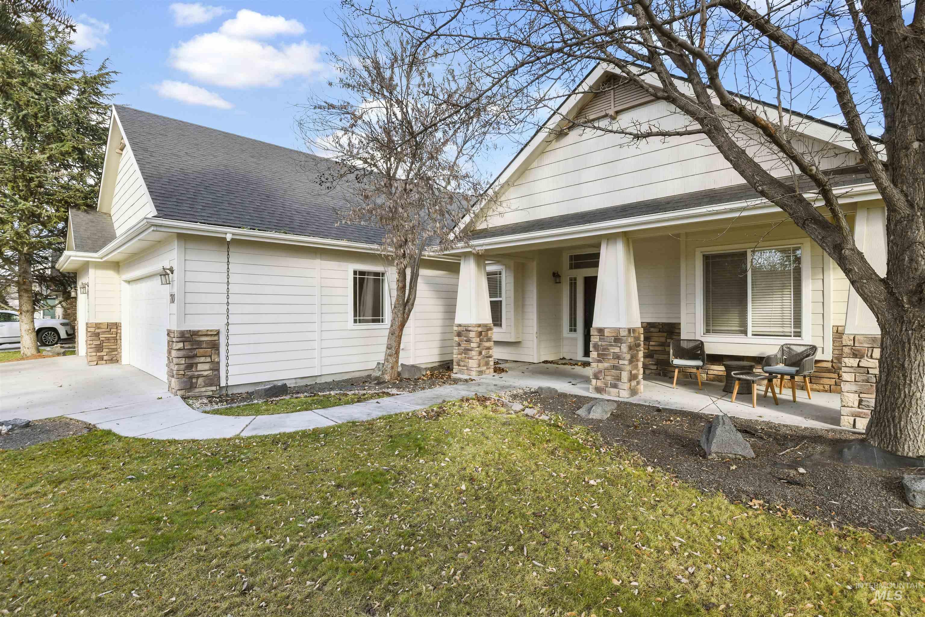 View of front facade featuring stone siding, roof with shingles, a front yard, concrete driveway, and a patio