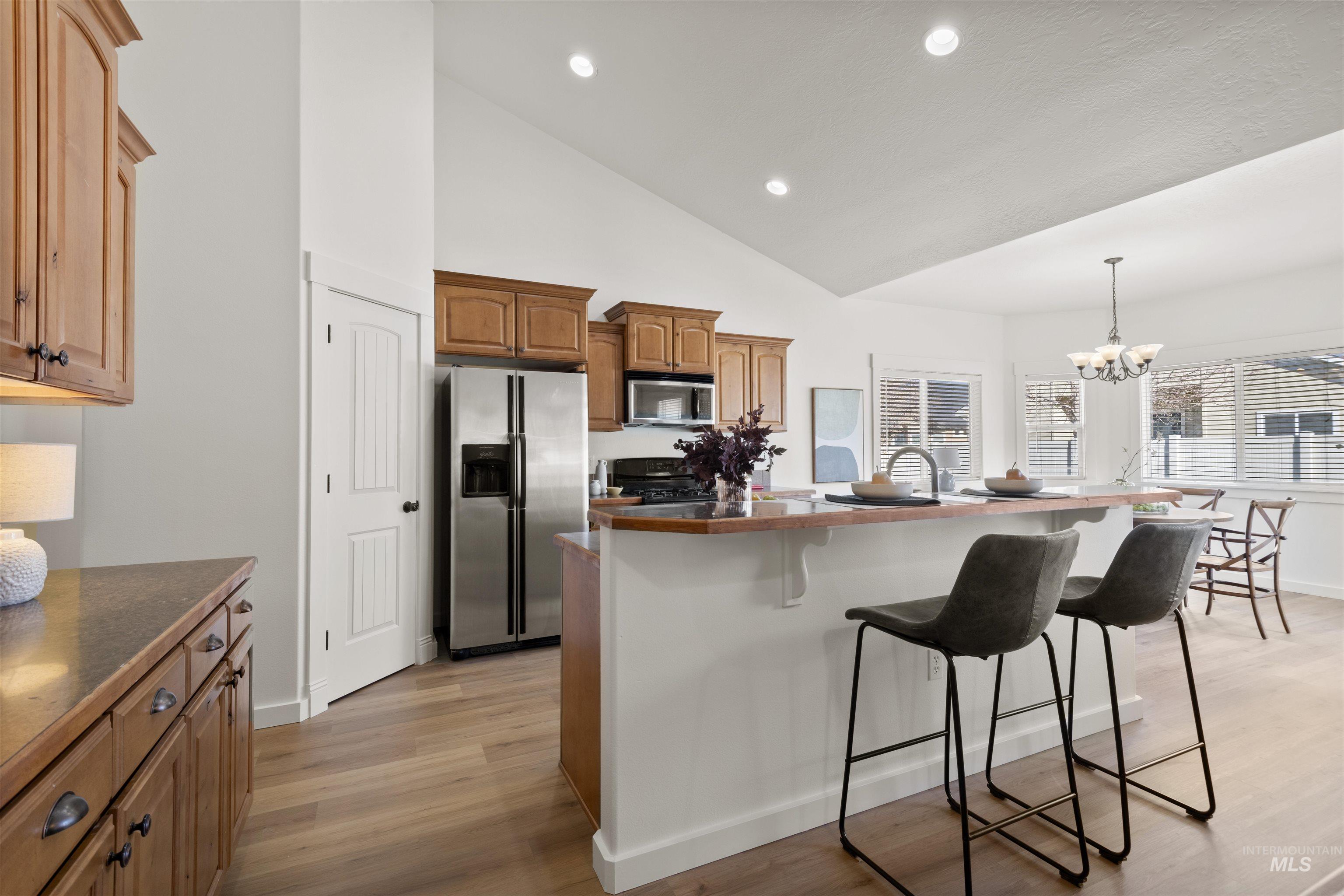 Kitchen featuring a breakfast bar, decorative light fixtures, high vaulted ceiling, stainless steel appliances, and a kitchen island with sink