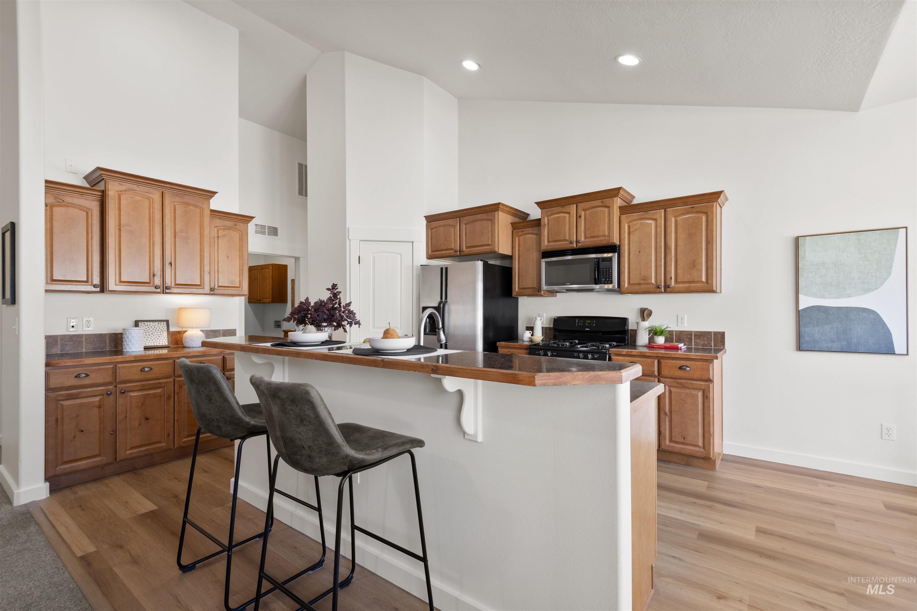 Kitchen featuring a breakfast bar area, brown cabinetry, an island with sink, appliances with stainless steel finishes, and light wood finished floors